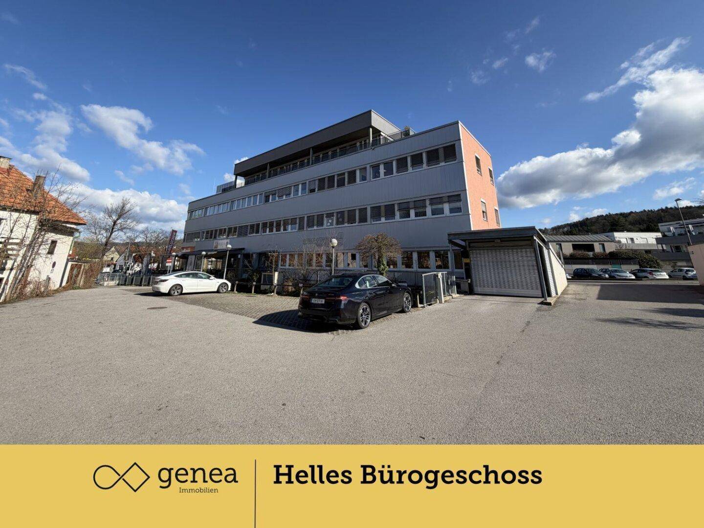 Rückansicht des Bürogebäudes mit großem Parkplatz und mehreren geparkten Fahrzeugen unter blauem Himmel.