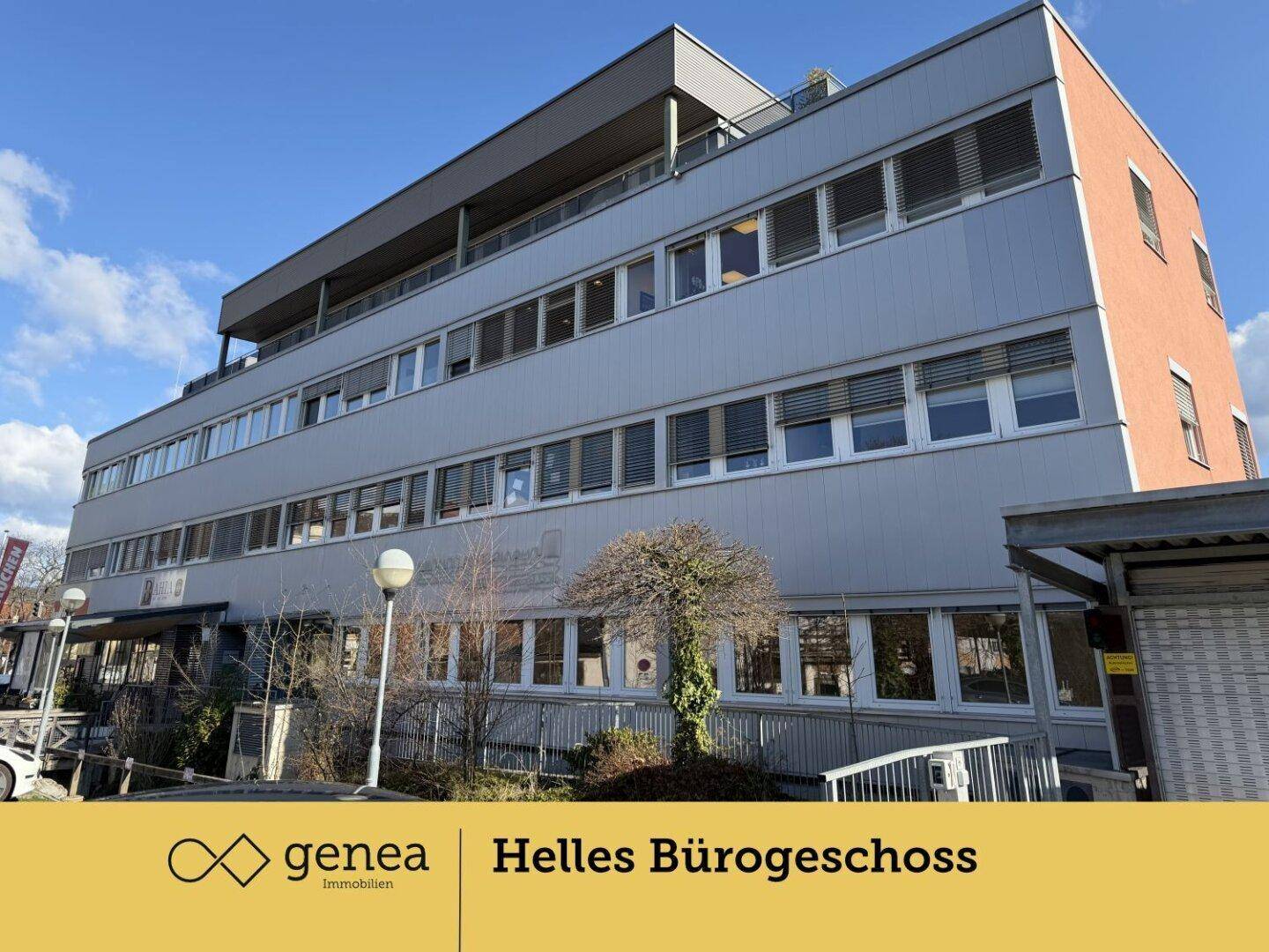 Frontansicht des Bürogebäudes mit vielen Fenstern und einem Eingangsbereich, umgeben von Bäumen.
