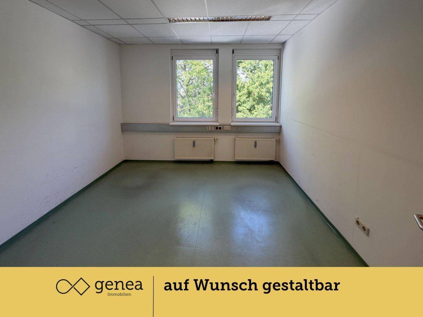 Leerer Büroraum mit hellen Wänden, grünem Boden und zwei Fenstern mit Blick ins Grüne.