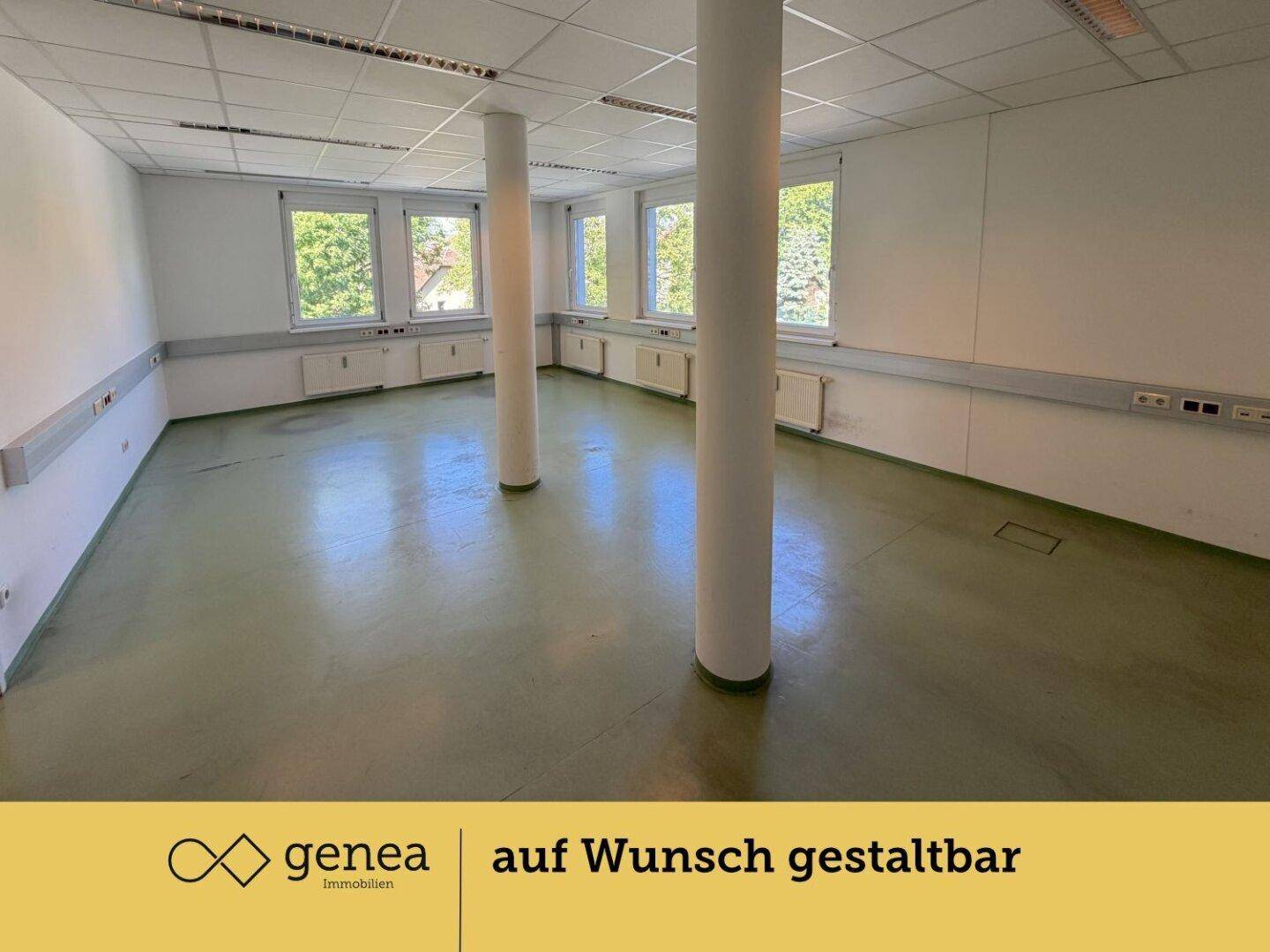 Großzügiger Büroraum mit mehreren Fenstern, zwei Säulen und grünem Bodenbelag.