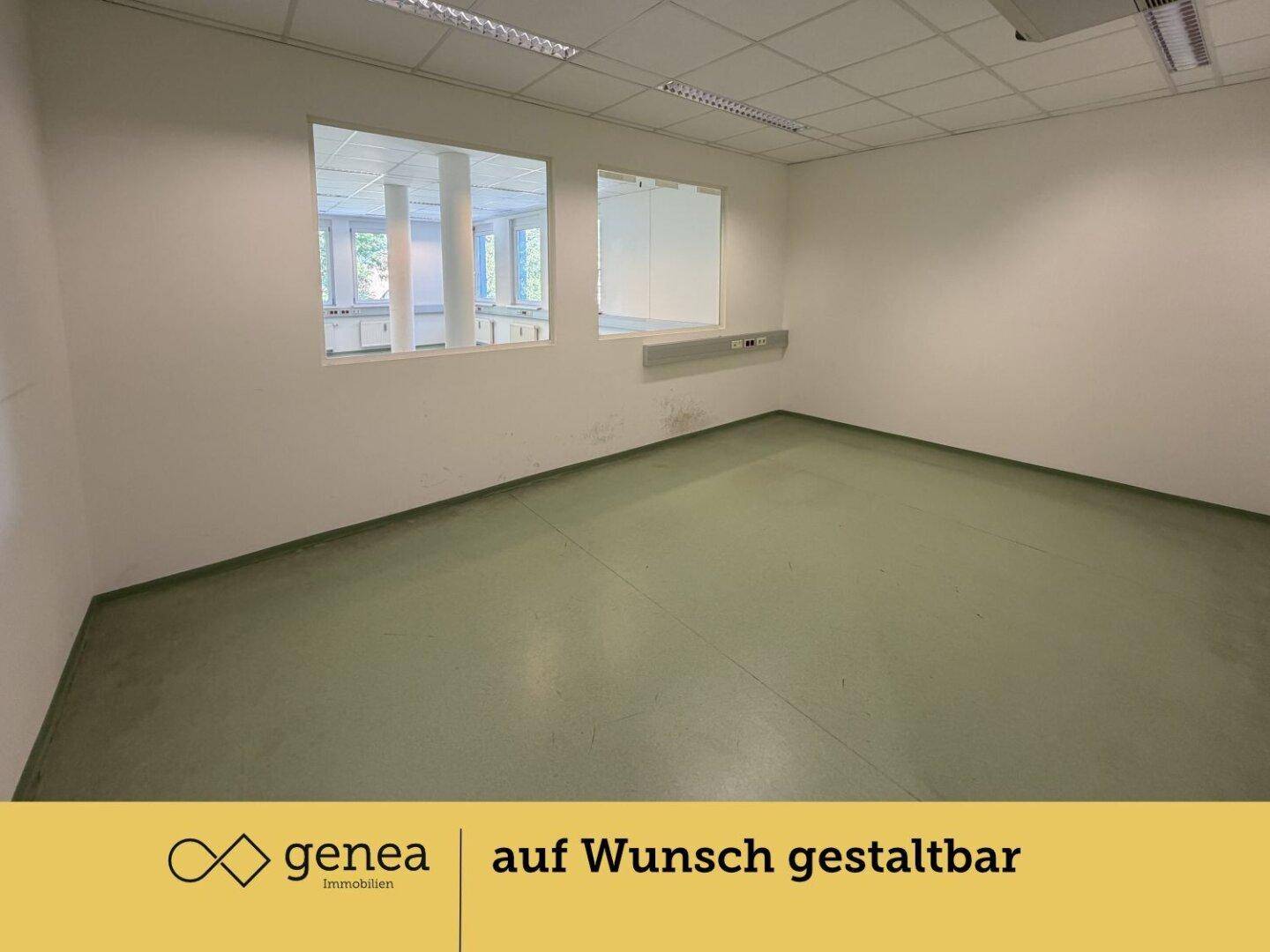 Büroraum mit Blick auf einen Innenhof durch große Fenster und grünem Bodenbelag.