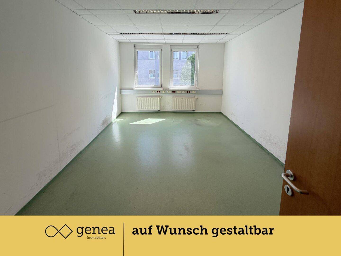 Leerer Büroraum mit grünem Boden, hellen Wänden und Fenstern mit Blick ins Grüne.