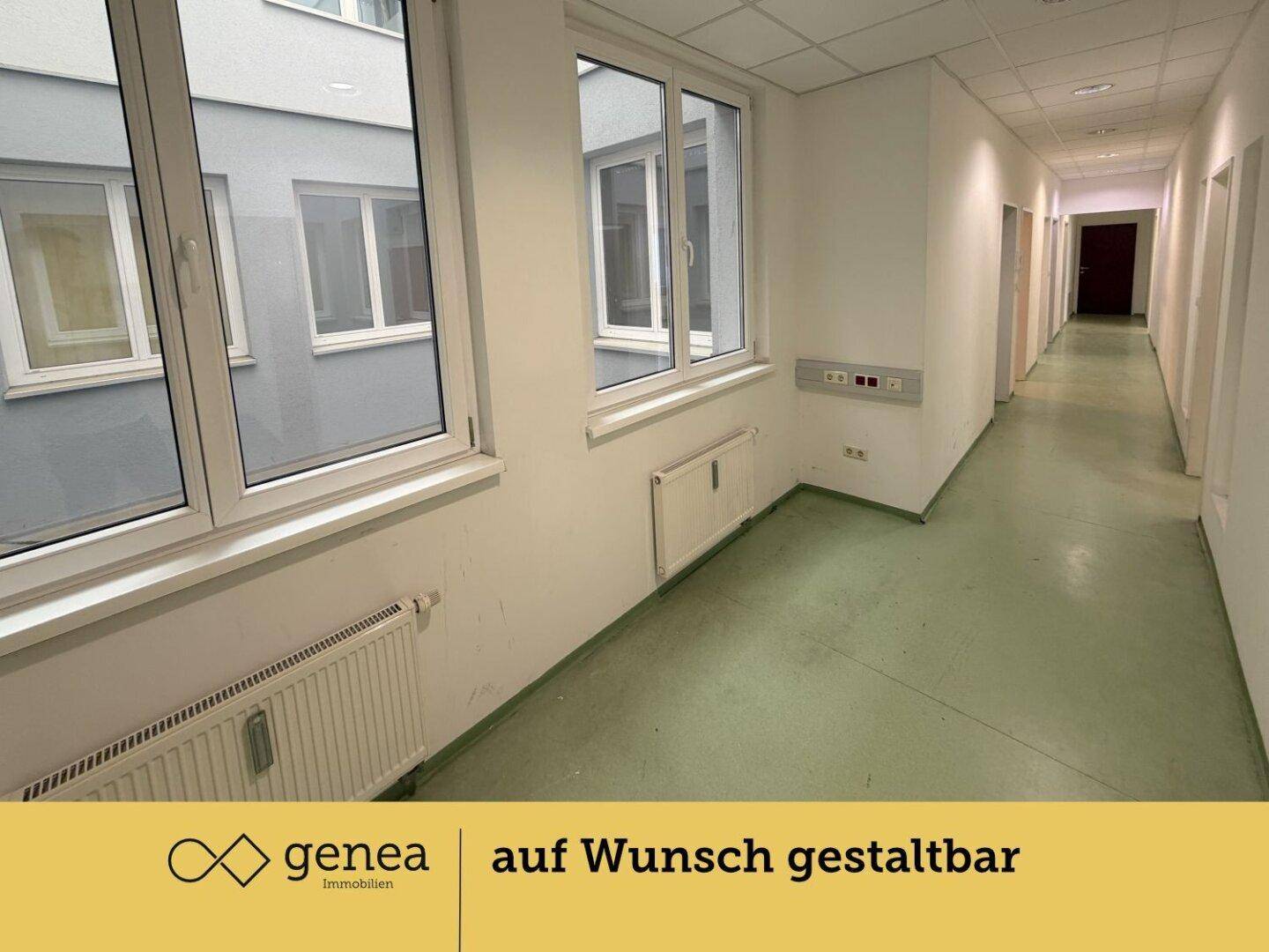 Langer Flur mit Fenstern zum Innenhof und Zugang zu mehreren Büroräumen, gut beleuchtet.