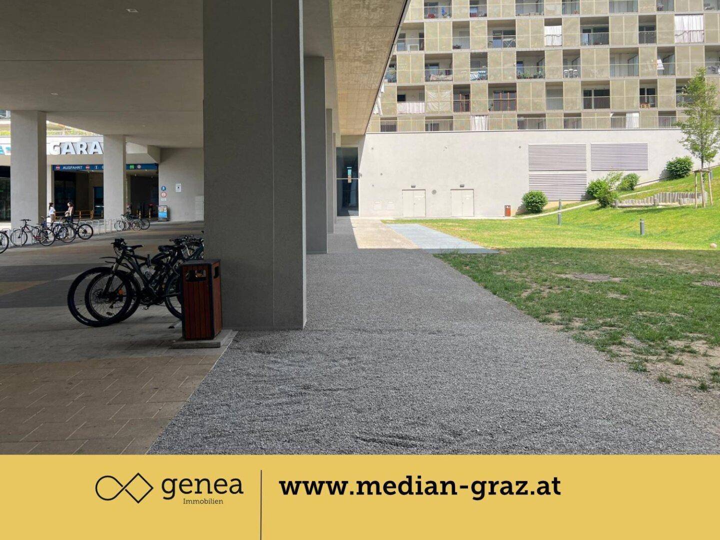 Eingangsbereich eines modernen Wohngebäudes mit Fahrradständern und Grünflächen.