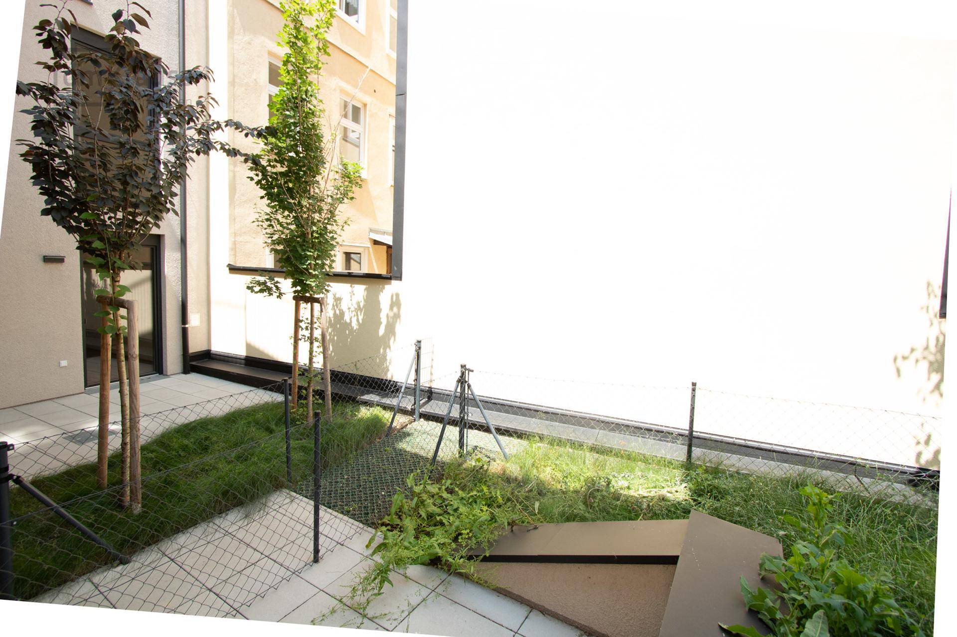 Unmöblierte Terrasse mit Fliesenboden und angrenzender Grünfläche, bereit zur Gestaltung.
