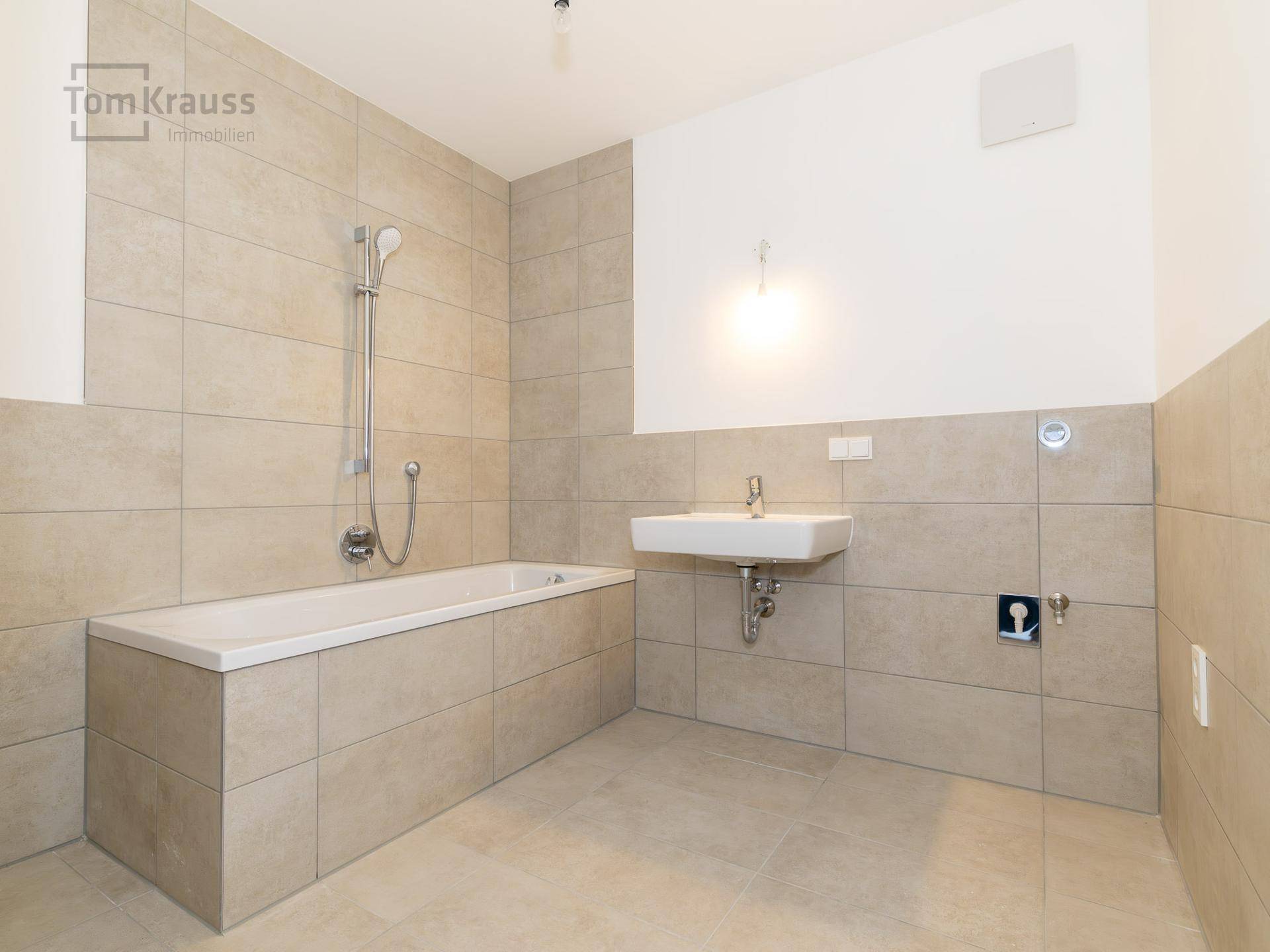 Modernes Badezimmer mit beigefarbenen Fliesen, Badewanne mit Duschfunktion und Waschbecken.