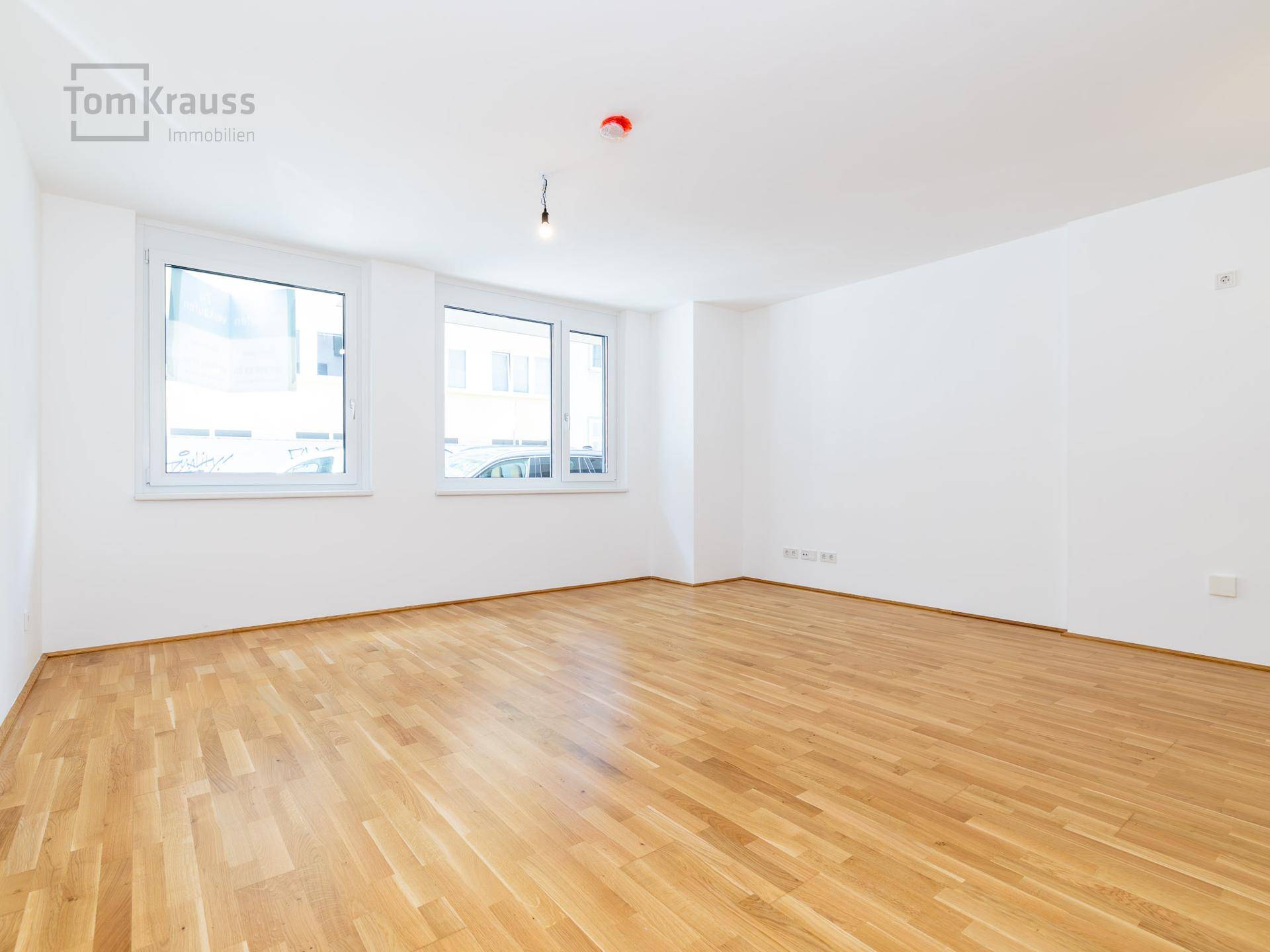 Geräumiges, leeres Zimmer mit hellem Parkettboden und drei großen Fenstern, ideal für Wohnzwecke.