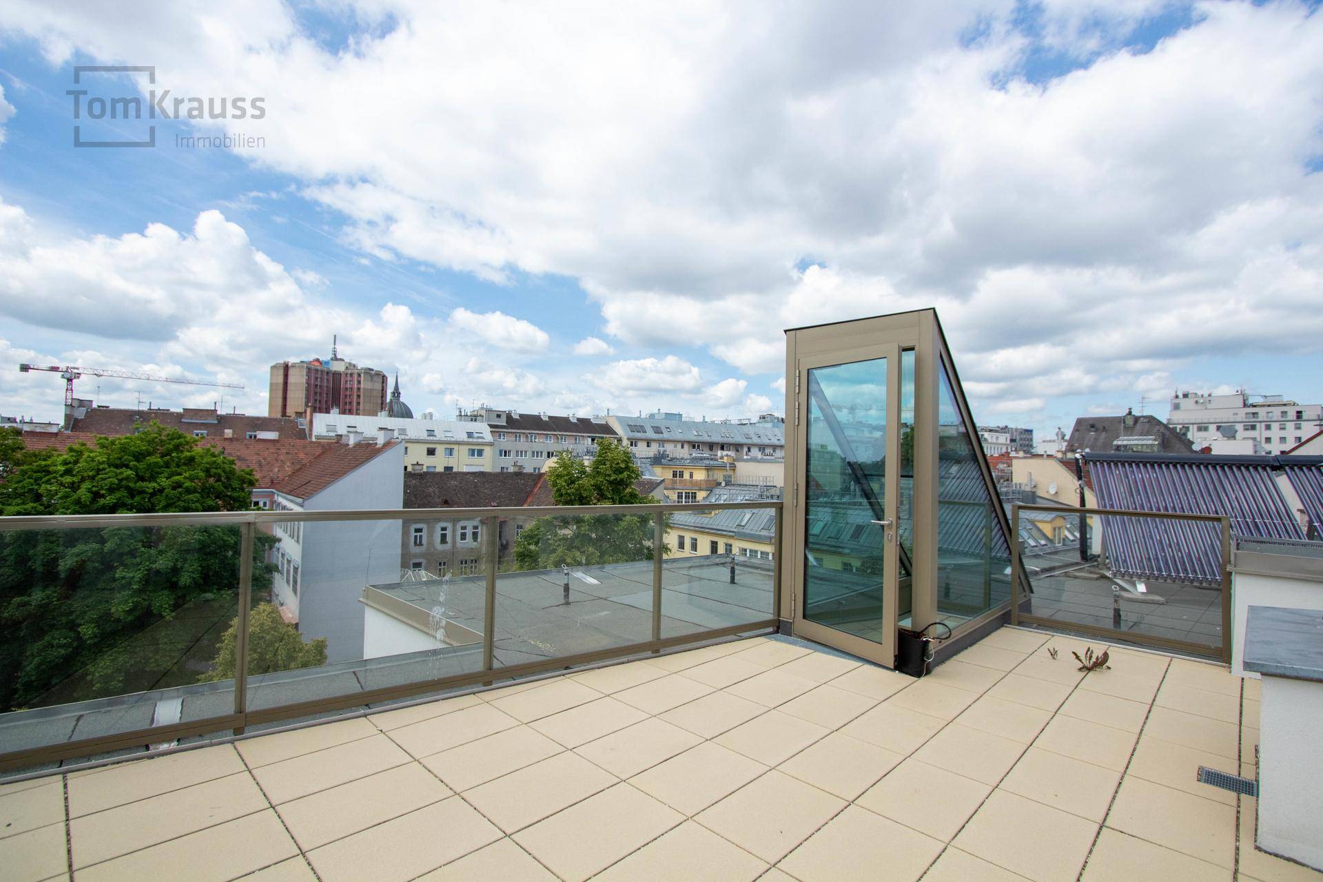 Dachterrasse mit Fliesenboden, Glasgeländer und einer modernen Glasstruktur mit Stadtblick.