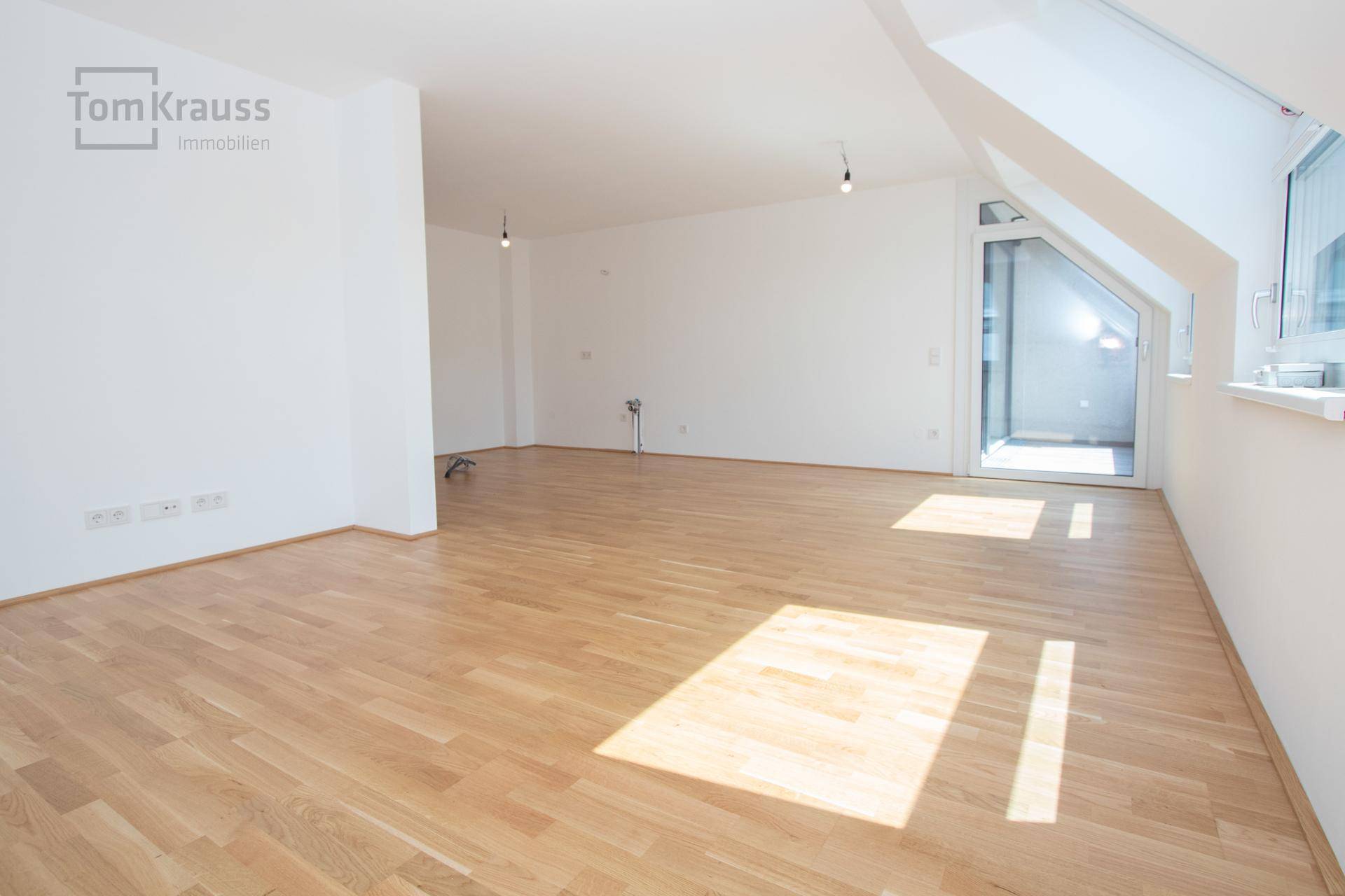 Heller, leerer Wohnbereich mit Holzparkett, Dachfenstern und Zugang zu einem Balkon.