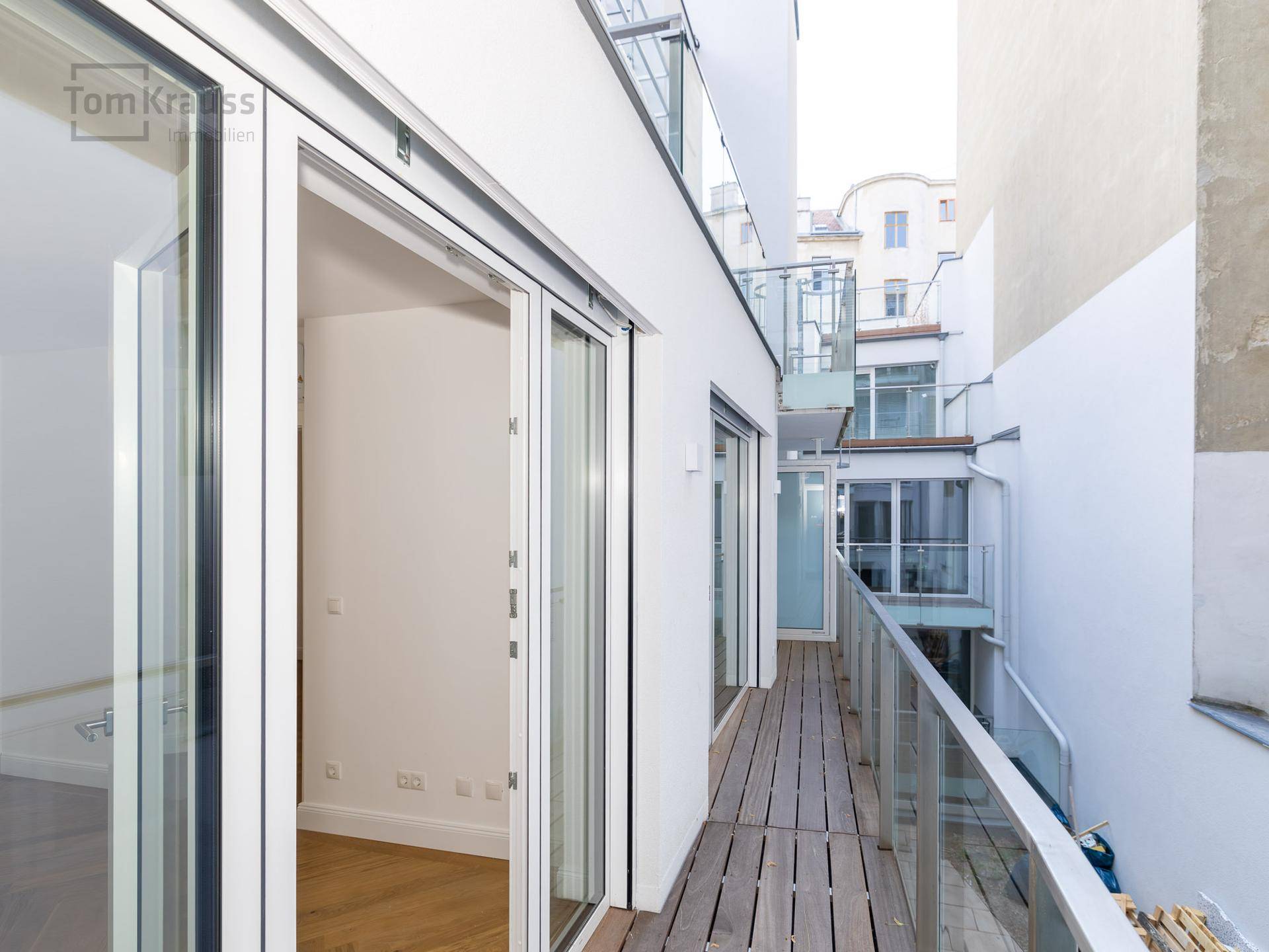 Langer Balkon mit Holzbelag und modernem Glasgeländer, der einen Außenbereich bietet.