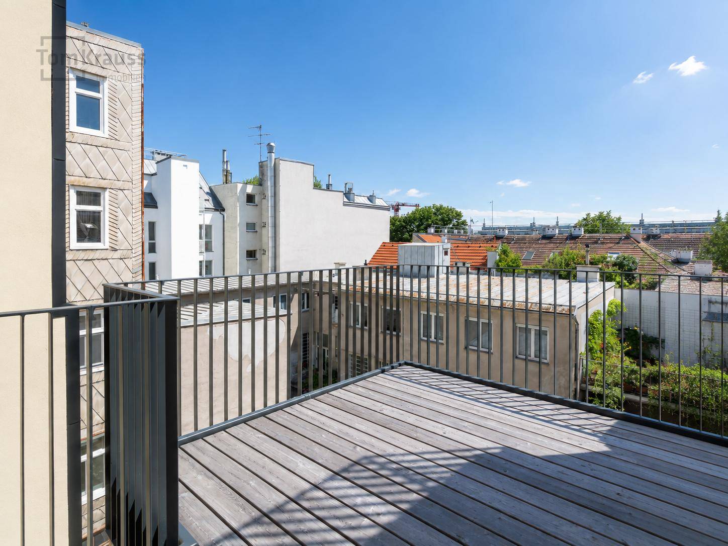 Geräumiger, unmöblierter Balkon mit Holzboden und Blick auf die umliegenden Gebäude.