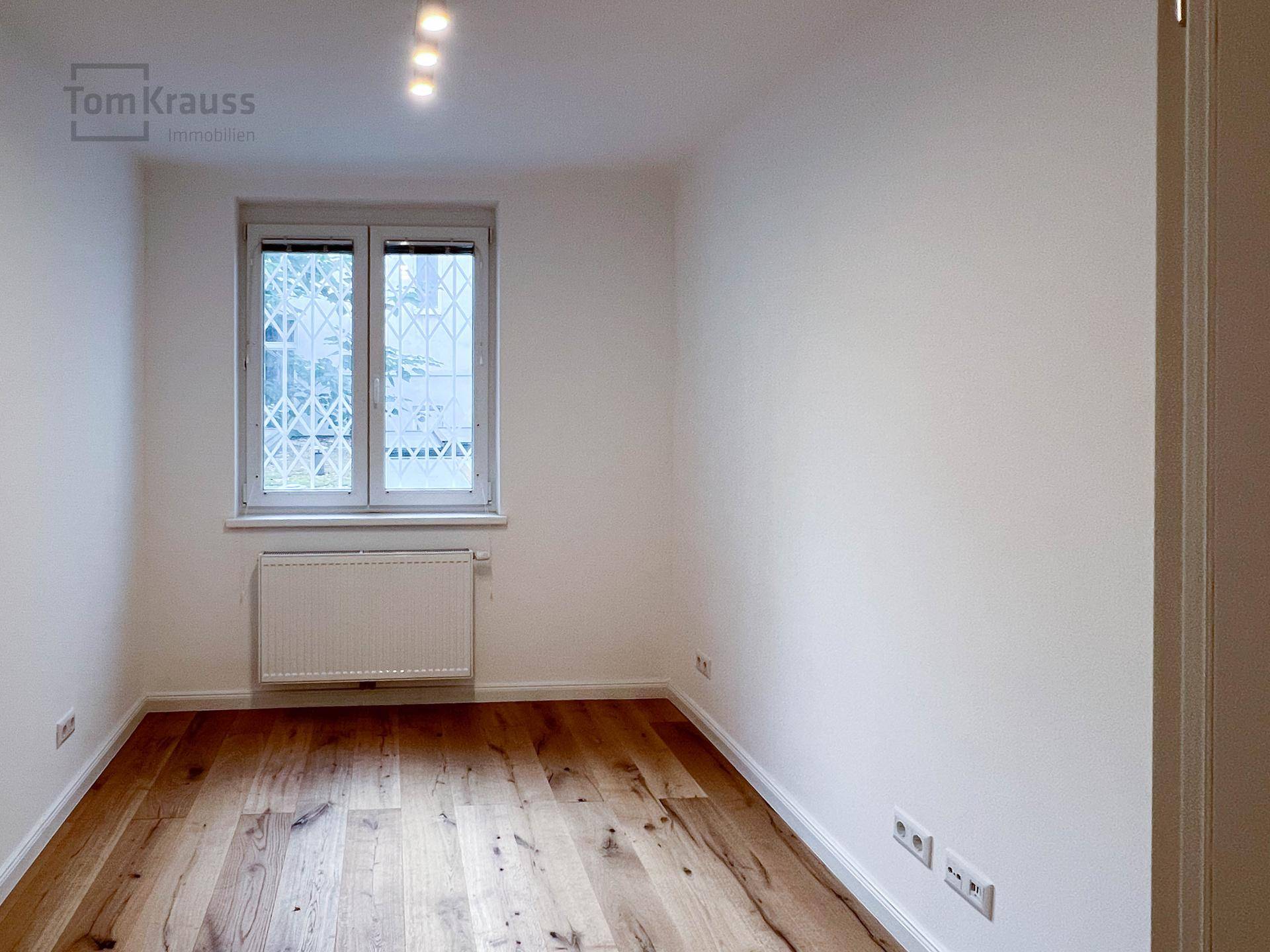Helles Zimmer mit Holzboden, weiß gestrichenen Wänden und Fenster.