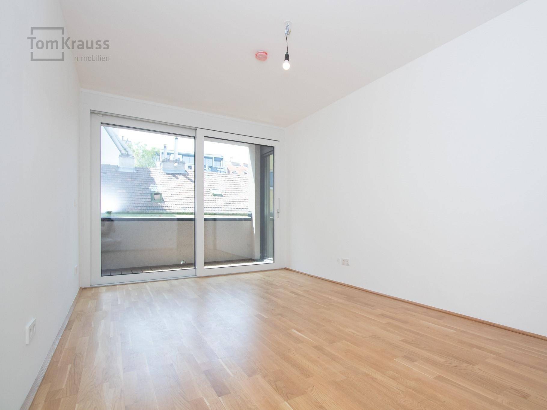 Heller, leerer Raum mit Parkettboden und großen Schiebetüren, die zu einem Balkon führen.