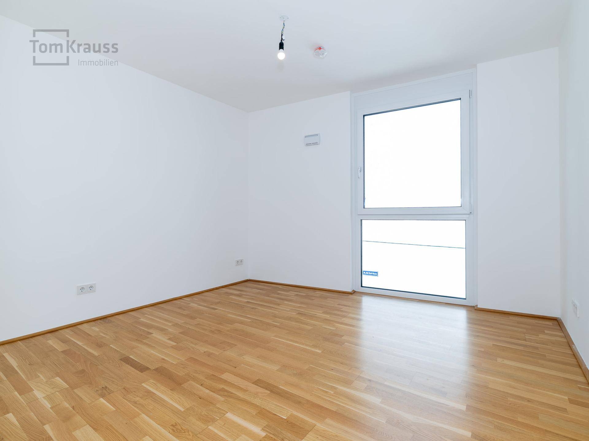 Heller, leerer Raum mit Parkettboden und großem Fenster, ideal für individuelle Gestaltung.