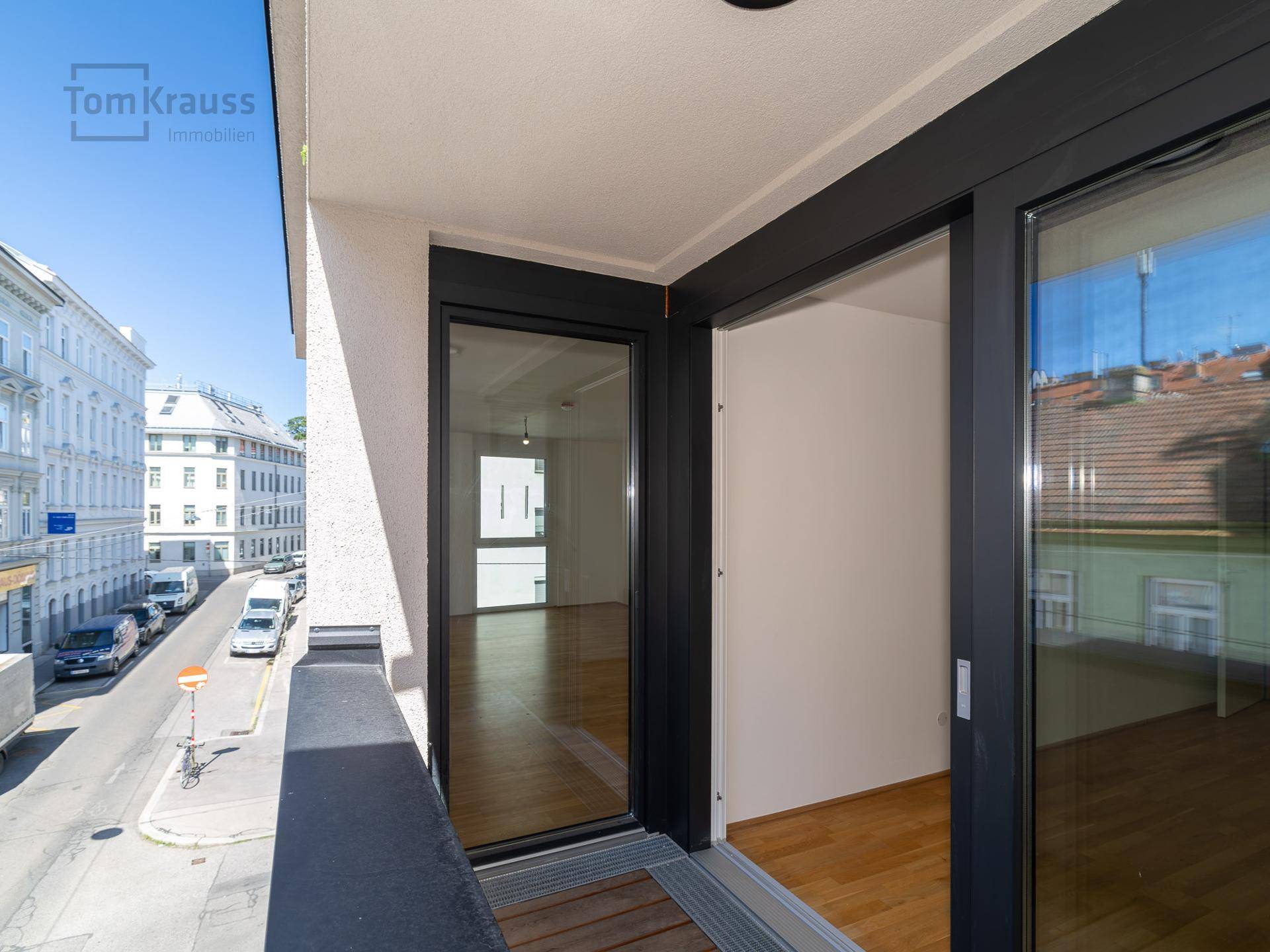Leerer Balkon mit Holzboden und Schiebetüren, bietet einen weiten Blick auf die Stadtstraße.