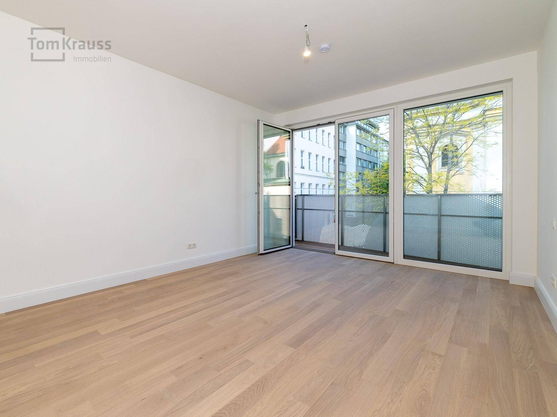 Helles Zimmer mit Holzboden und großen Fenstern, die einen Blick auf die Umgebung bieten.