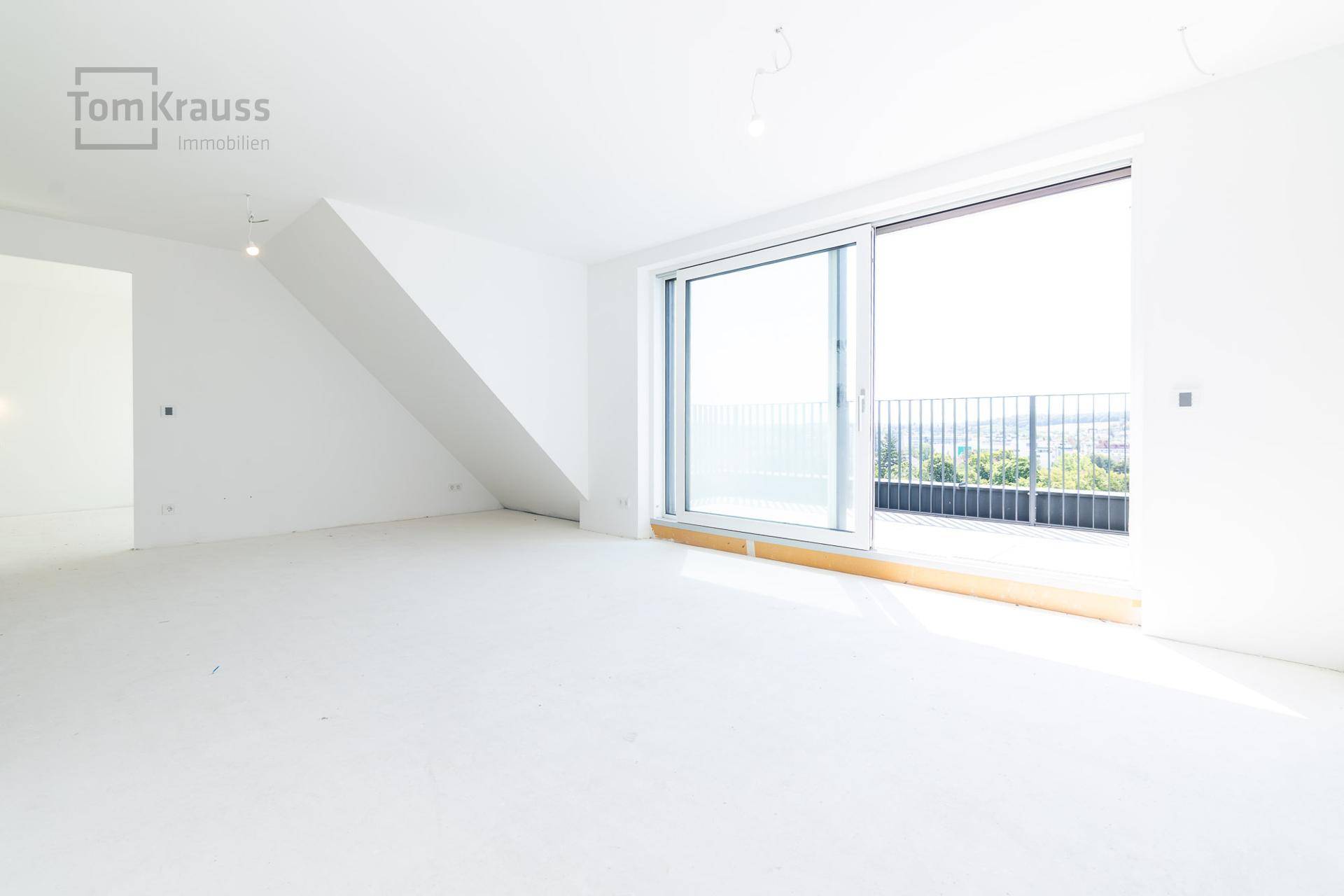 Unmöblierter Raum mit großen Fenstern und Zugang zu einem Balkon mit Panoramablick.