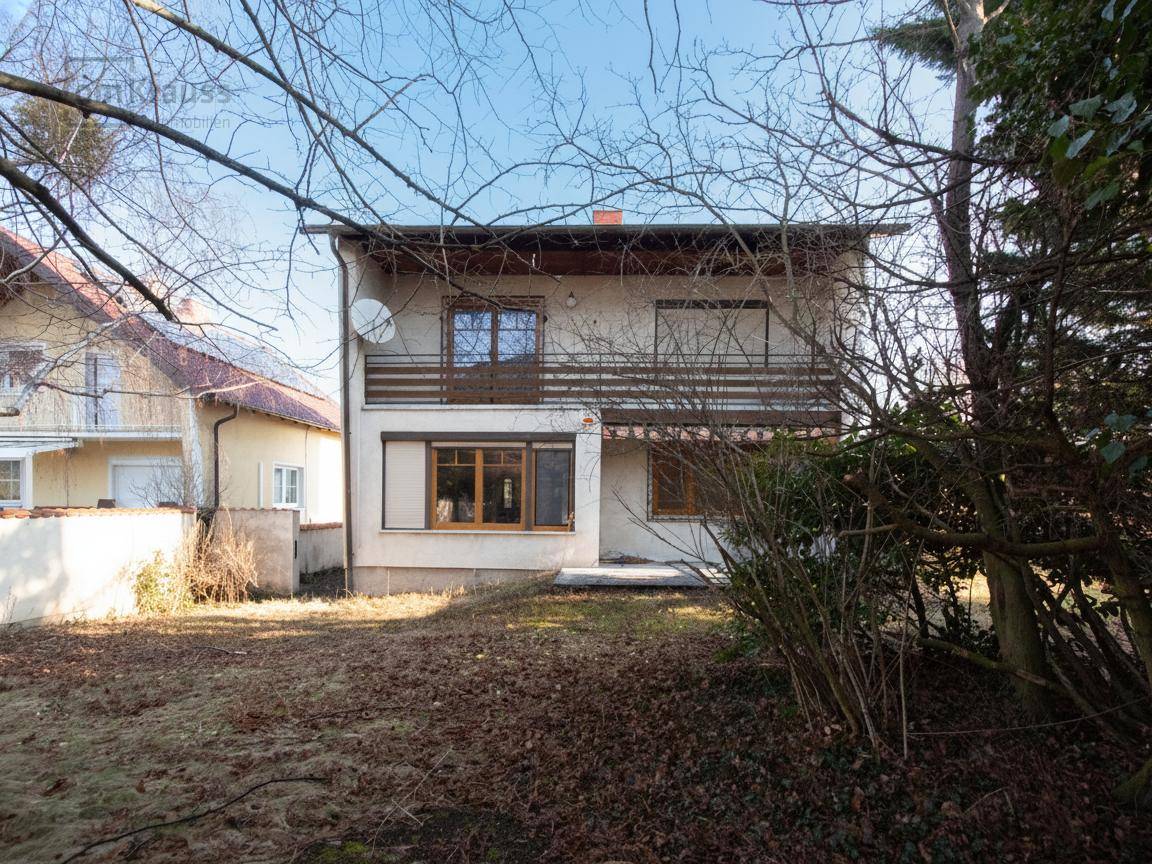 Hinteransicht des Hauses mit großem, naturbelassenem Garten und Balkon im Obergeschoss.