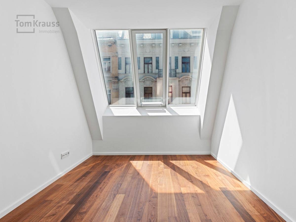 Helles Zimmer mit Holzboden und großer Fensterfront, die einen Blick auf die Stadt bietet.