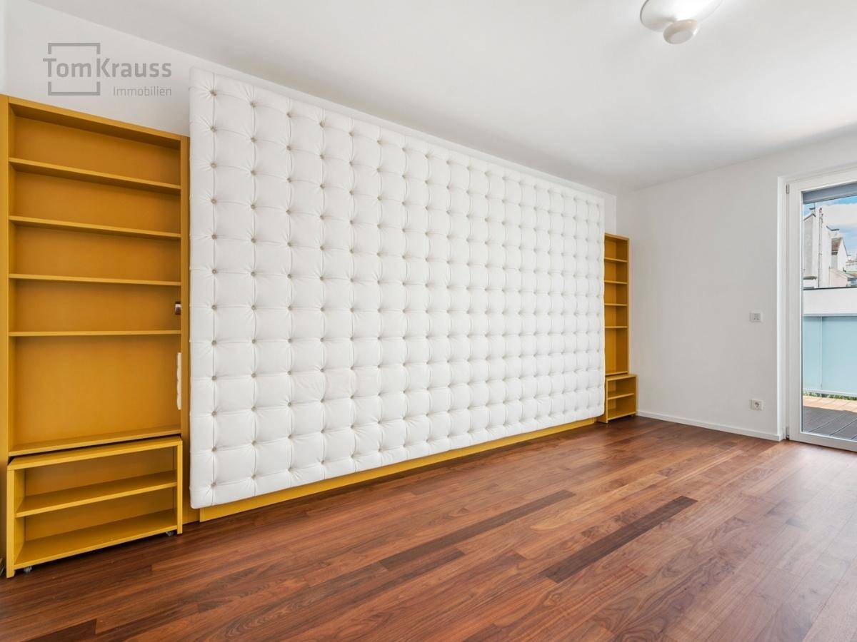 Geräumiges Zimmer mit Holzboden, gelben Regalen und einer gepolsterten Wand.