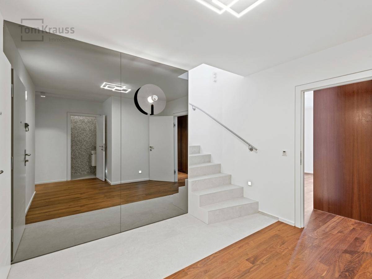 Heller Eingangsbereich mit moderner Treppe, großem Spiegel und Holzboden.