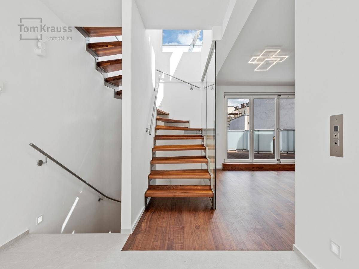 Eingangsbereich mit moderner Holztreppe, Glasgeländer und integriertem Aufzug.