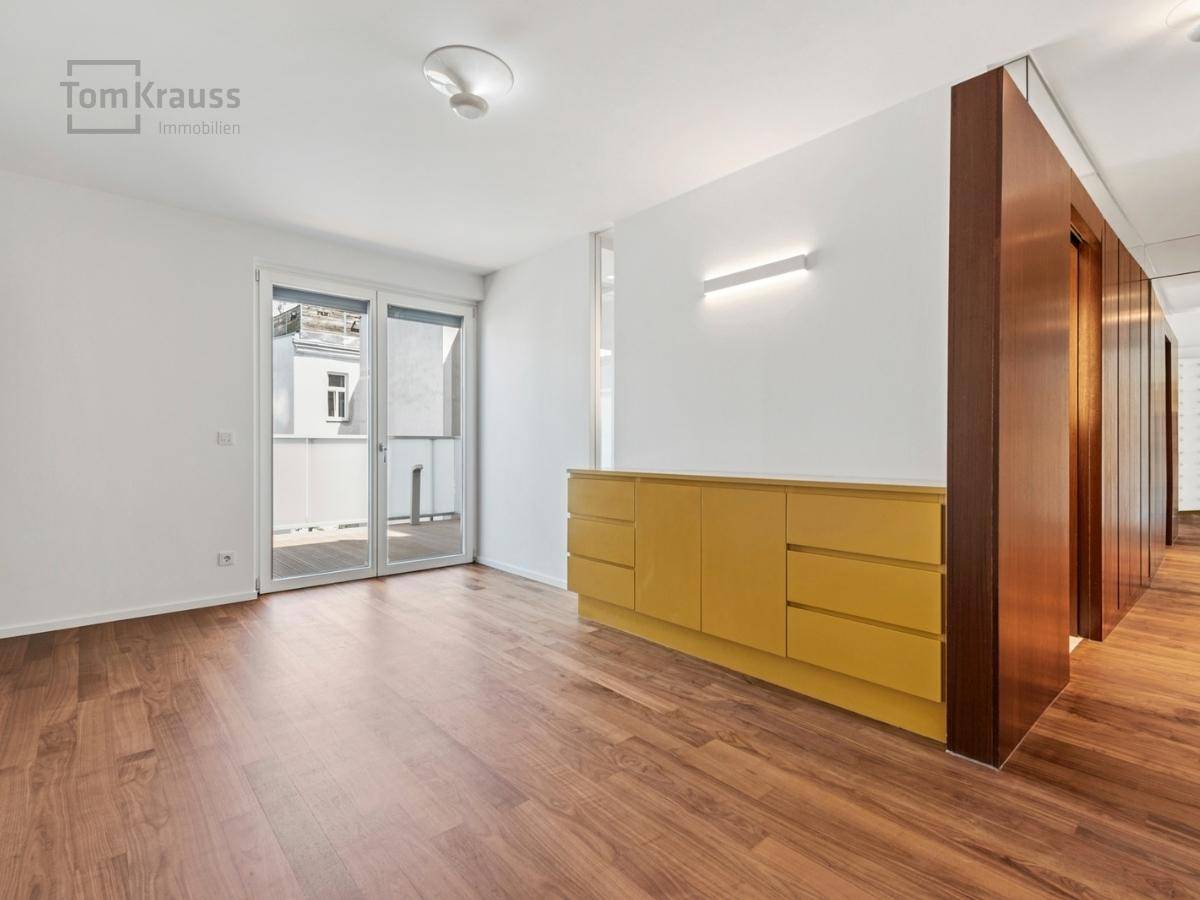 Heller Raum mit Holzboden, gelbem Sideboard und Zugang zu einem Balkon.