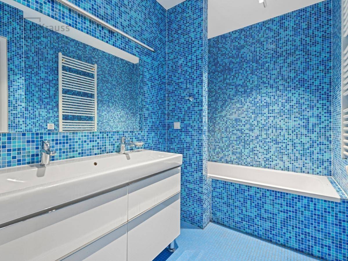 Modernes Badezimmer mit blauen Mosaikfliesen, Doppelwaschbecken und Badewanne.