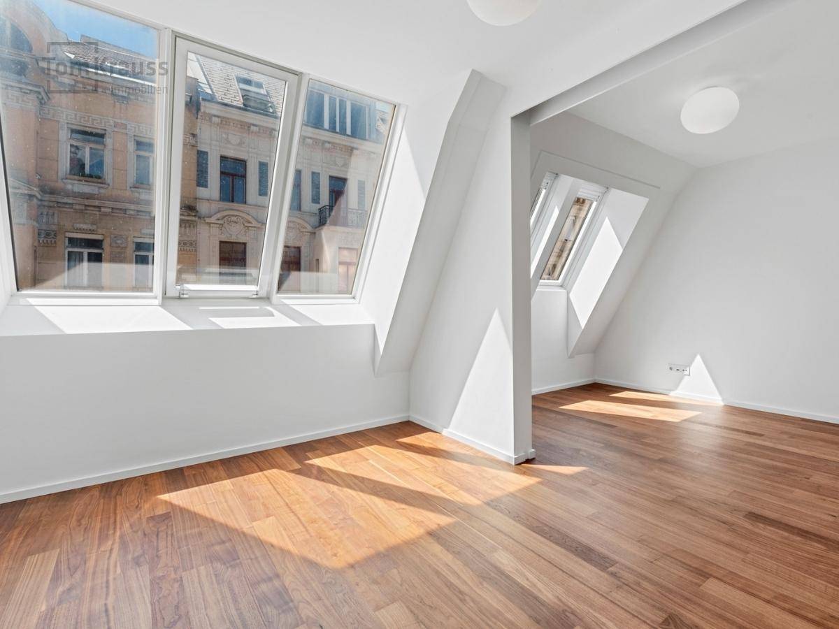 Helles Zimmer mit Holzboden, Dachfenstern und Blick auf die historische Architektur.