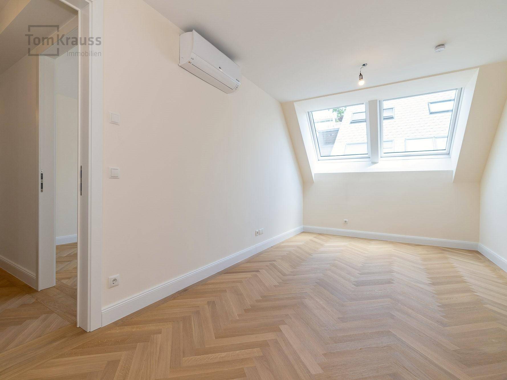 Helles Schlafzimmer mit Fischgrätparkett, Dachfenstern und Klimaanlage, bereit zur Einrichtung.