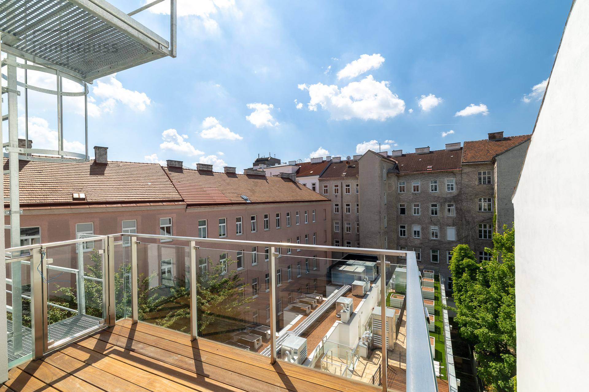 Balkon mit Holzboden und Glasgeländer bietet einen weiten Blick über die umliegenden Gebäude.