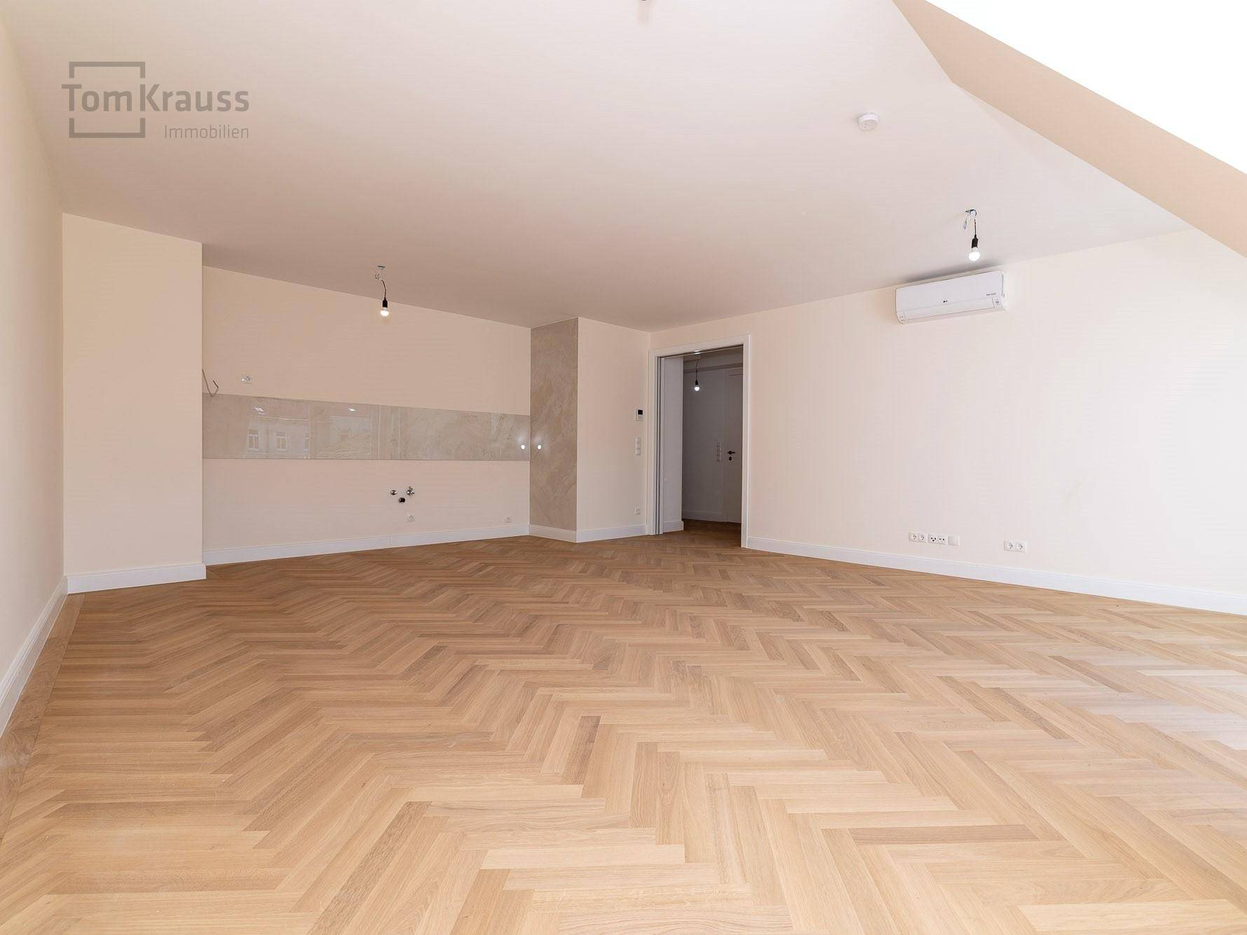 Geräumiger, heller Raum mit Fischgrätparkett und Vorbereitung für eine moderne Einbauküche.