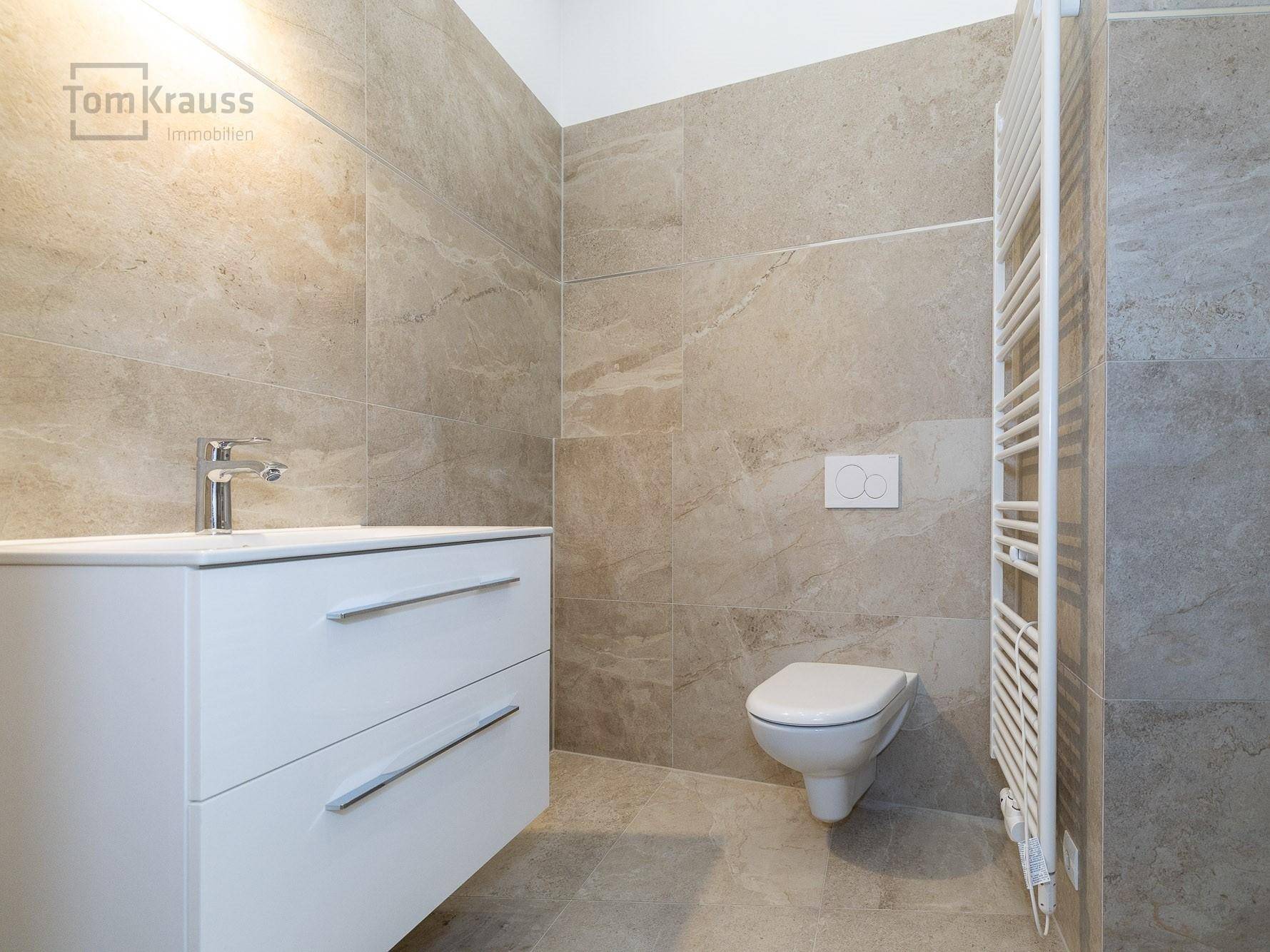 Modernes Badezimmer mit beigefarbenen Fliesen, wandhängendem WC und Waschtischunterschrank.