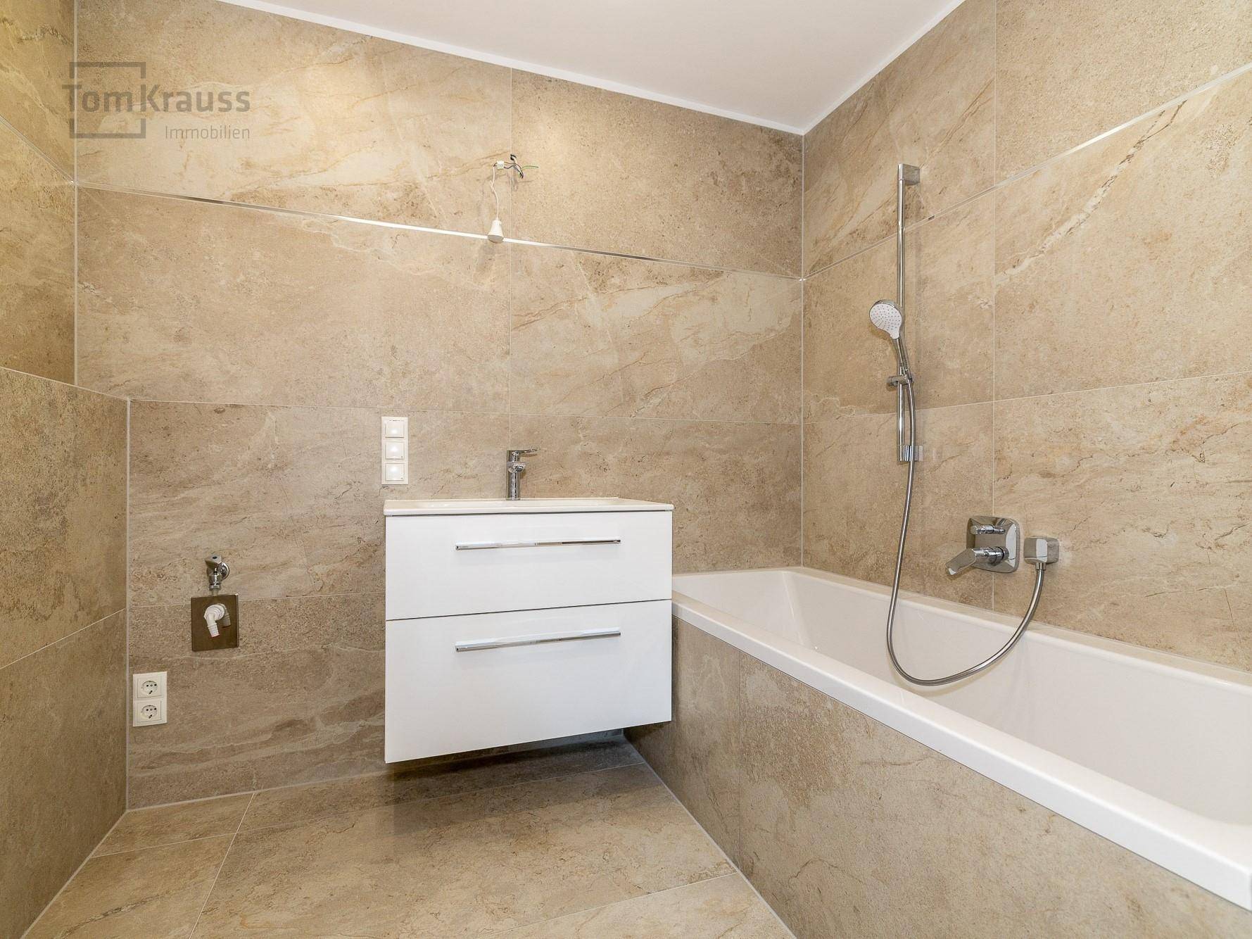 Modernes Badezimmer mit beigefarbenen Fliesen, Waschtisch und integrierter Badewanne für entspannende Momente.