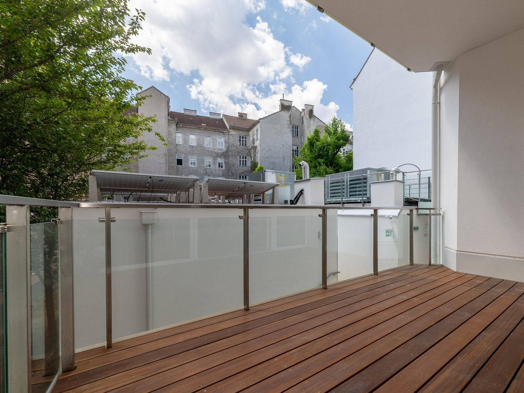 Geräumiger Balkon mit Holzbelag und Glasgeländer, bietet einen schönen Blick auf die Umgebung.