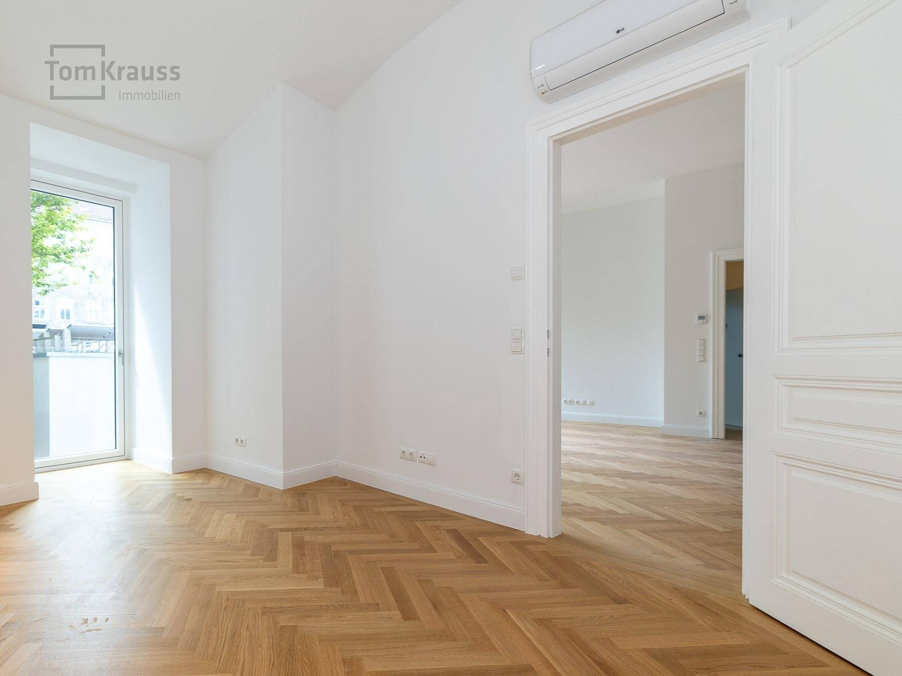 Helles Zimmer mit Fischgrätparkett, Klimaanlage und Zugang zu einem Balkon, ideal für erholsame Nächte.