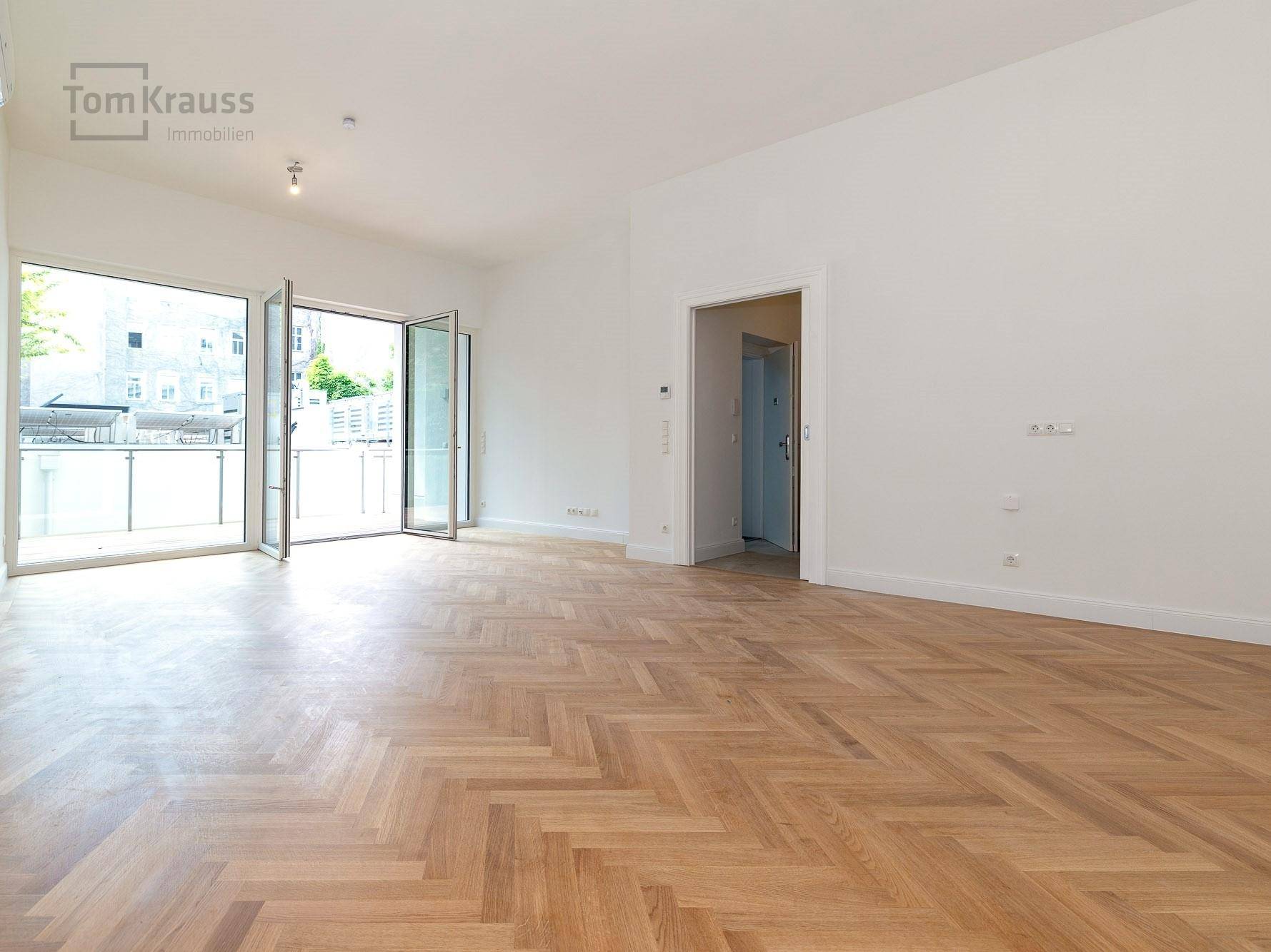 Heller Wohnbereich mit Fischgrätparkett und großen Fenstertüren, die viel natürliches Licht hereinlassen.