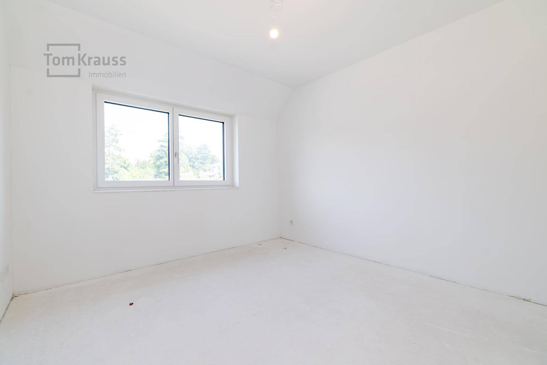Leeres Schlafzimmer mit weiß gestrichenen Wänden und einem großen Fenster.