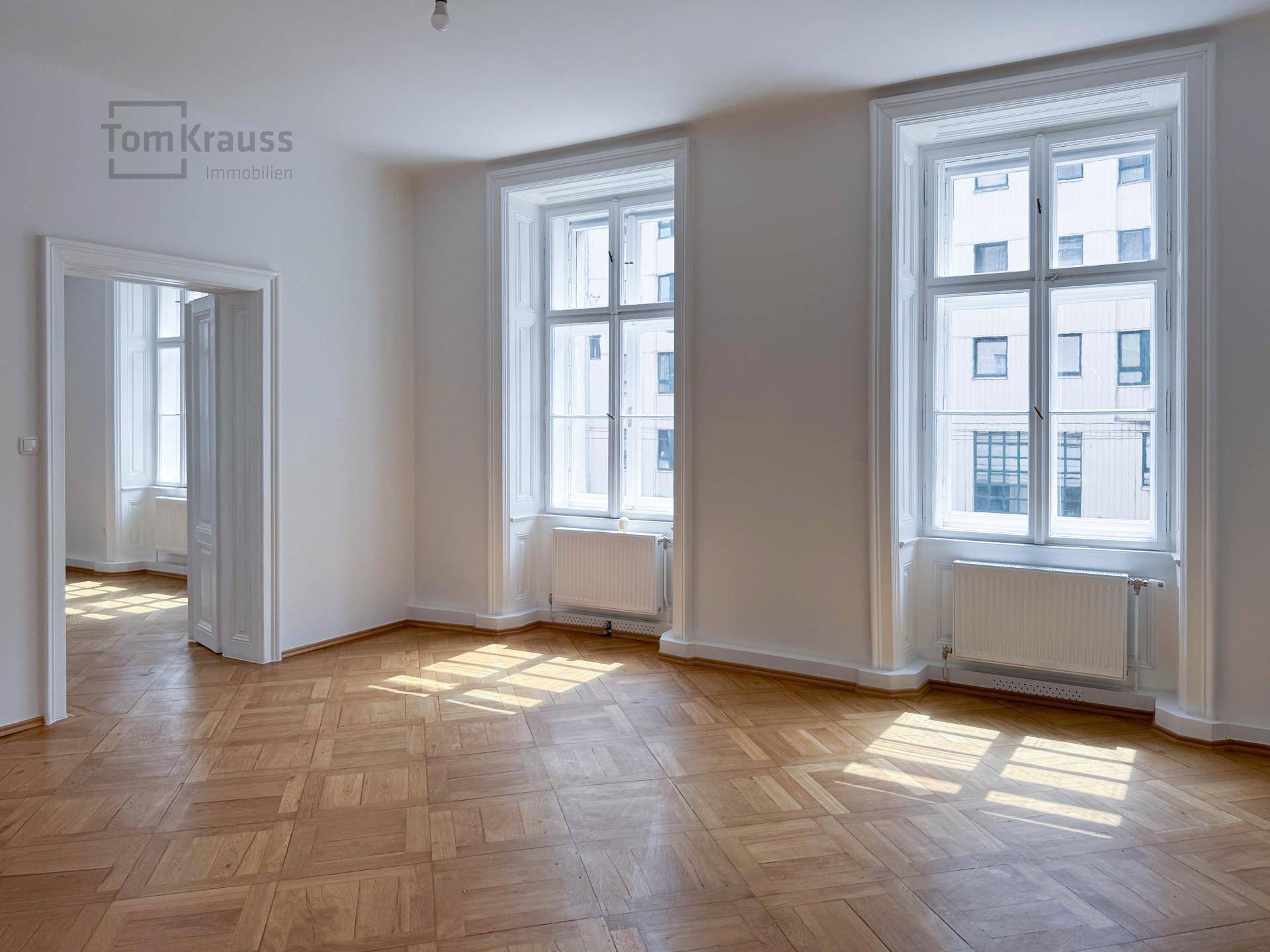 Großes, helles Zimmer mit Parkettboden und zwei hohen Fenstern, ideal für eine vielseitige Nutzung.