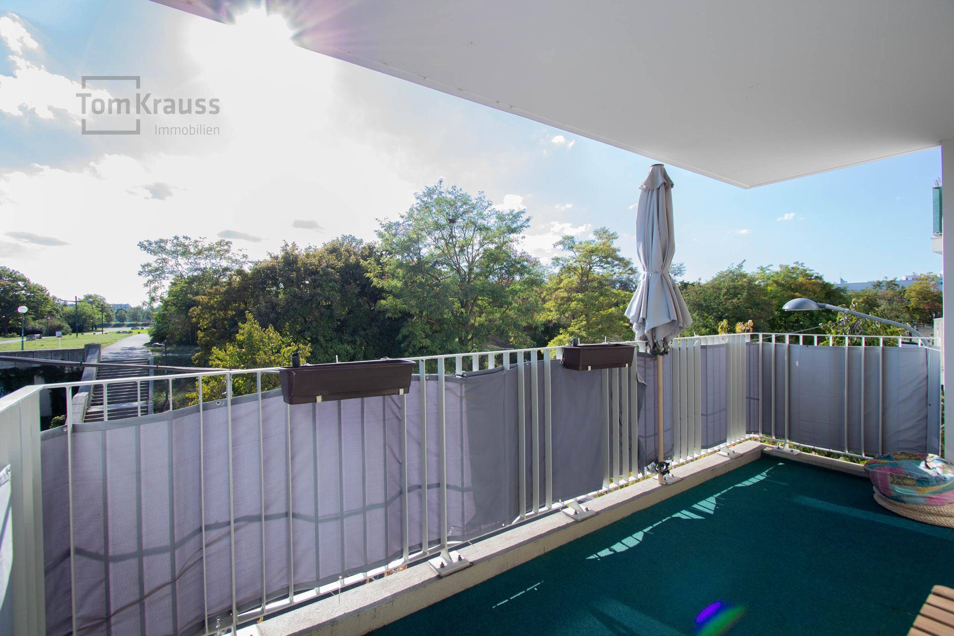 Heller Balkon mit Sonnenschirm und Blick auf die umliegende Grünfläche, bietet viel Privatsphäre.