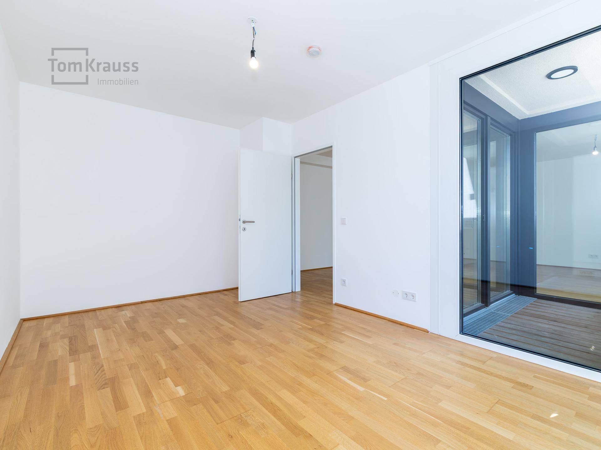 Geräumiger, heller Raum mit Holzboden und großen Fenstern, ideal für Wohnzwecke.