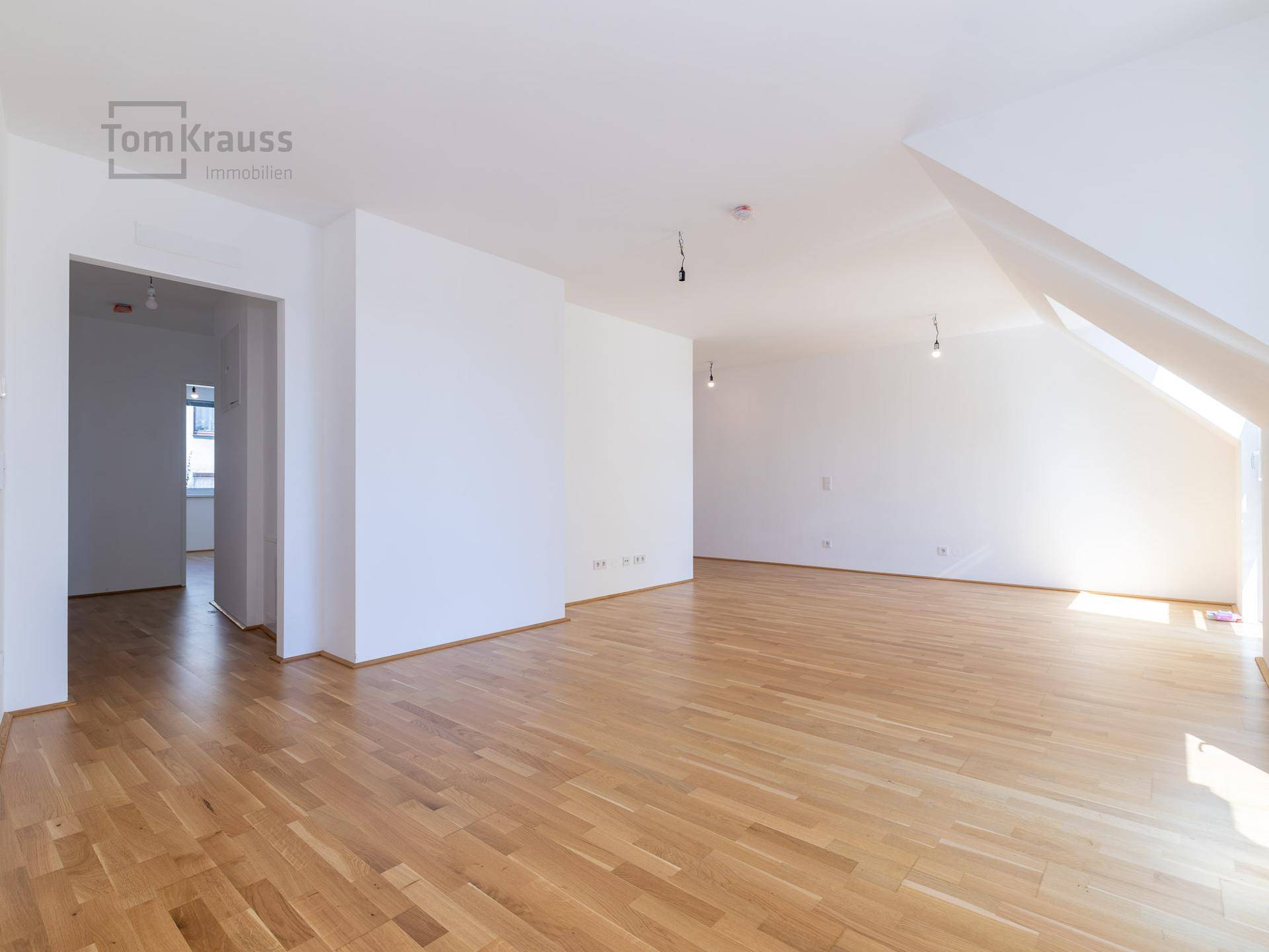 Heller, leerer Raum mit Holzboden und weißen Wänden, bereit zur individuellen Gestaltung.