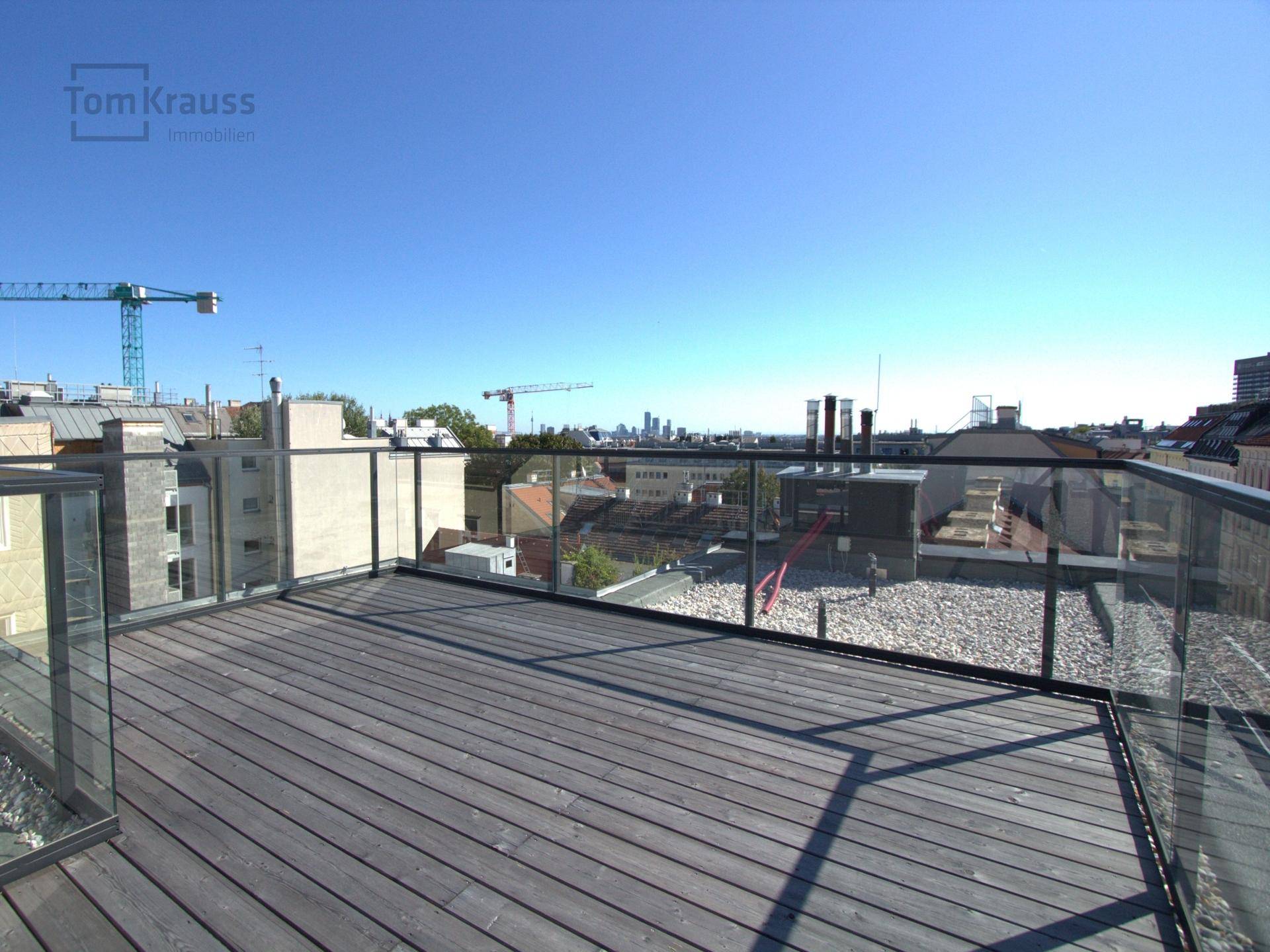 Geräumige Dachterrasse mit Glasgeländer und weitem Blick über die Stadt.