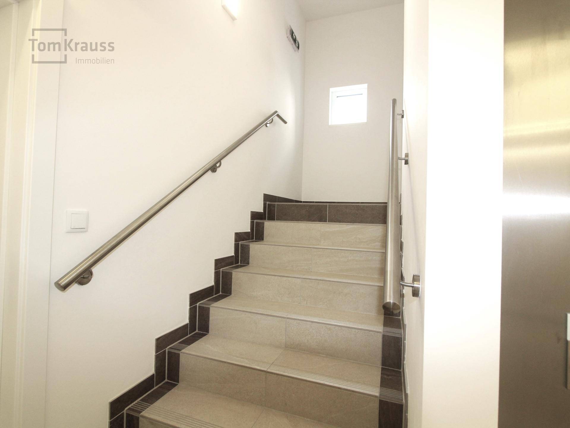 Modernes Treppenhaus mit Fliesenstufen und Edelstahlgeländer, neben dem Aufzug gelegen.