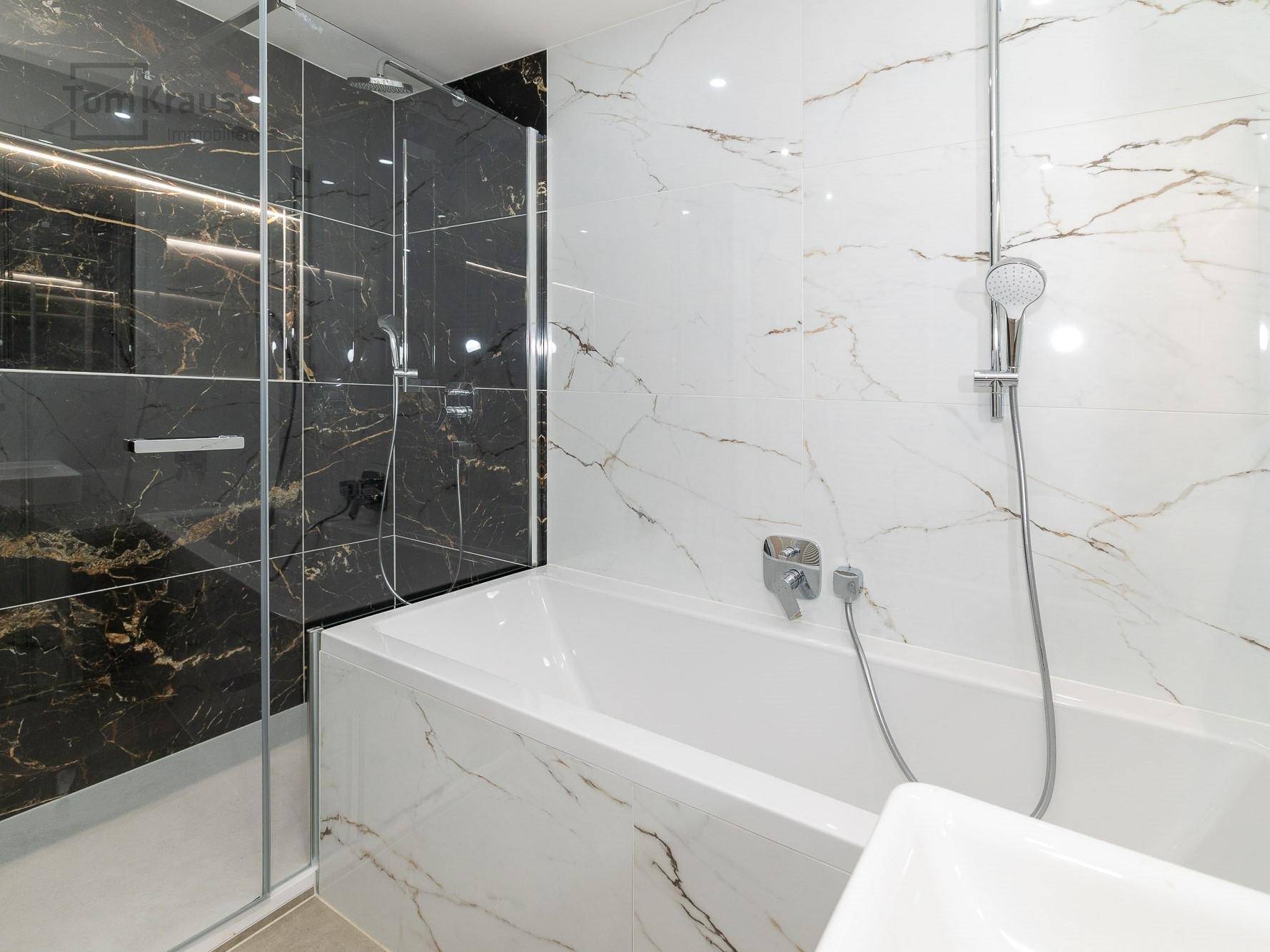 Luxuriöses Badezimmer mit schwarz-weißen Marmorfliesen, Badewanne und begehbarer Dusche.