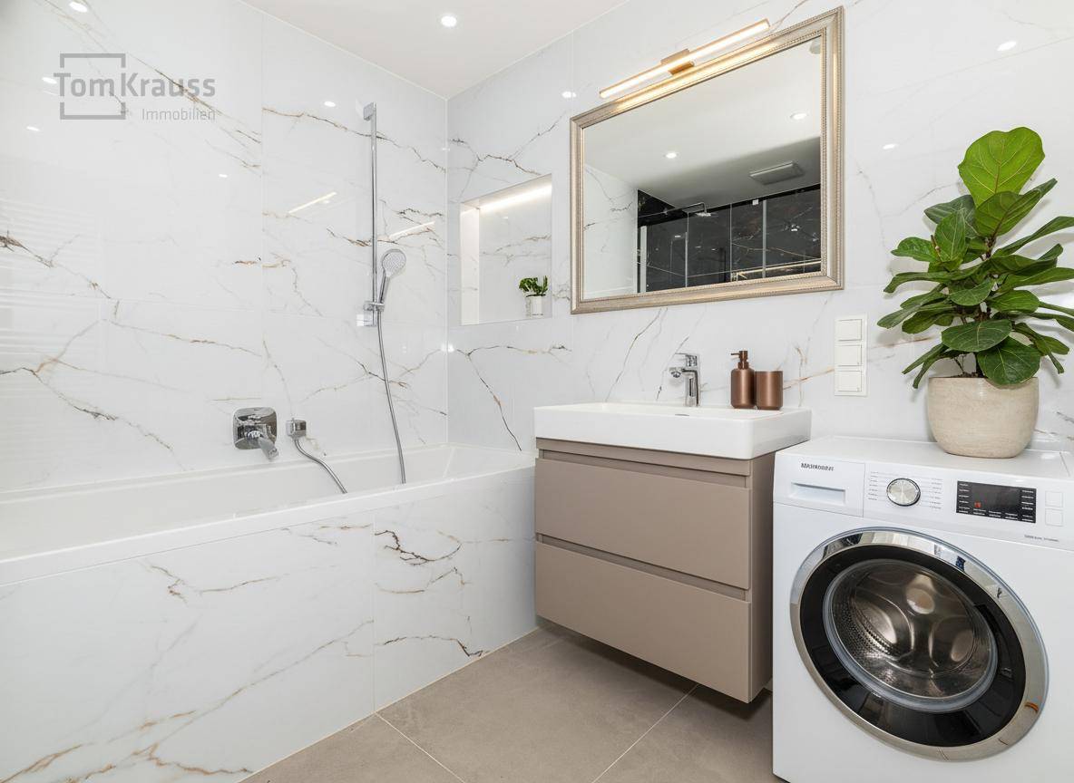 Stilvolles Badezimmer mit Badewanne, Waschtisch und integrierter Waschmaschine, alles in modernem Design.