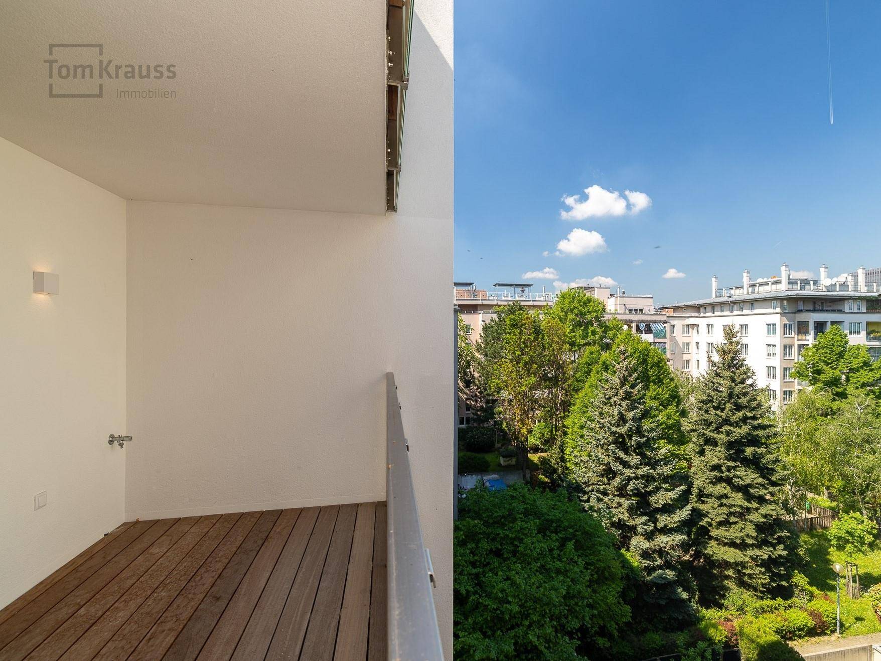 Heller Balkon mit Holzboden und weitem Blick ins Grüne und auf die Stadt.