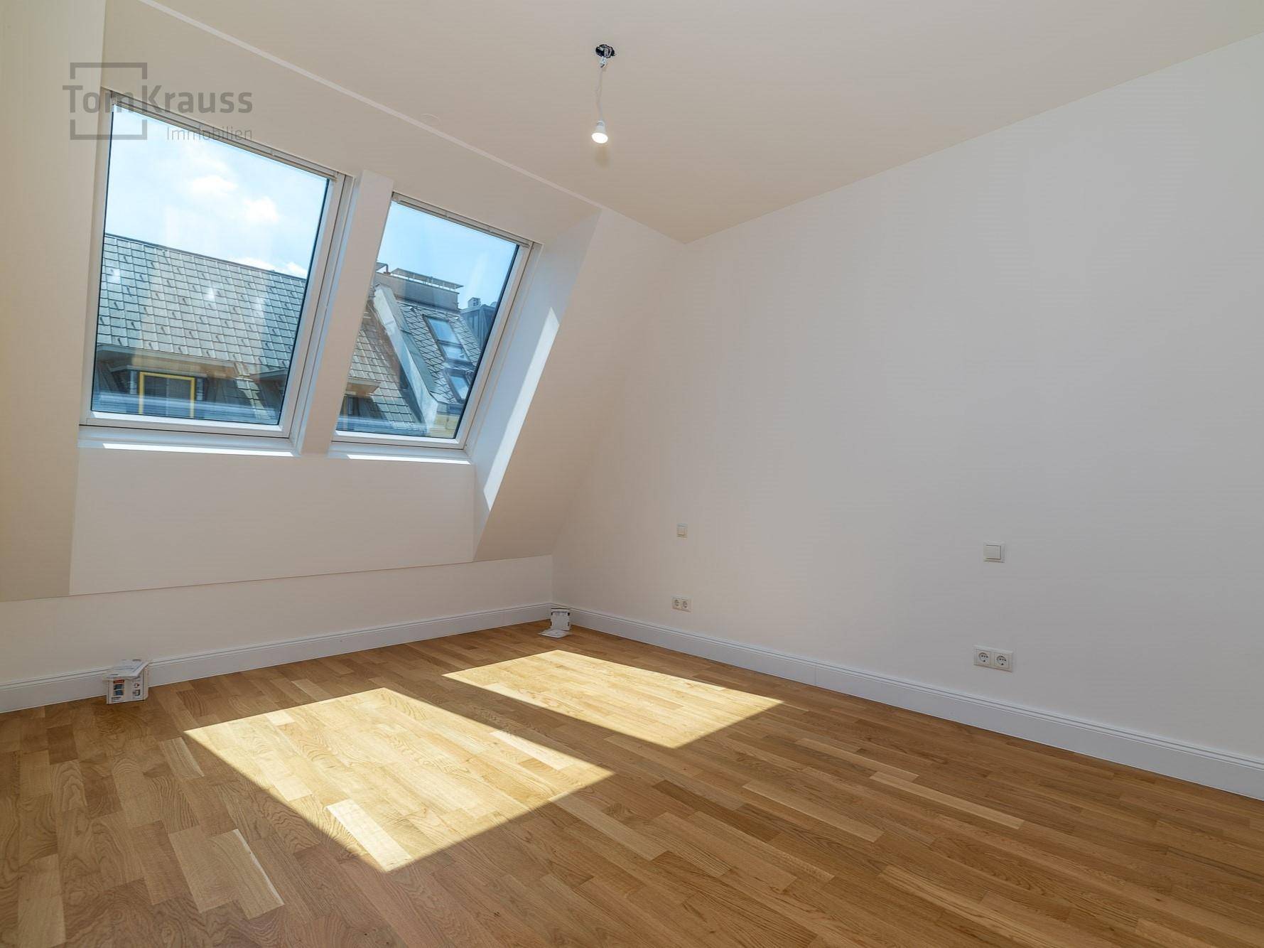 Helles, unmöbliertes Schlafzimmer mit Dachschrägen, Dachfenstern und Holzboden.