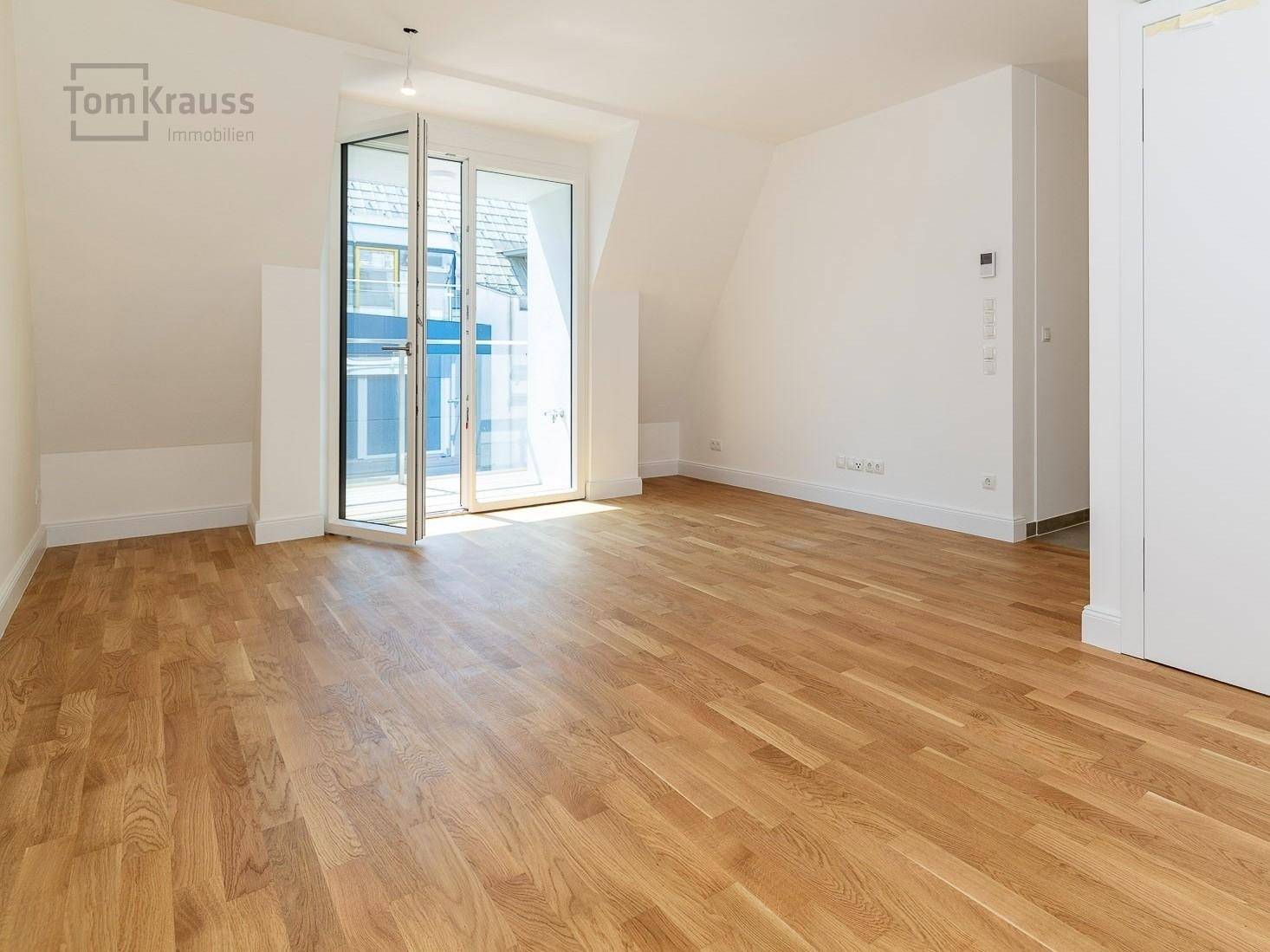 Geräumiges, unmöbliertes Wohnzimmer mit Holzboden und Zugang zum Balkon.