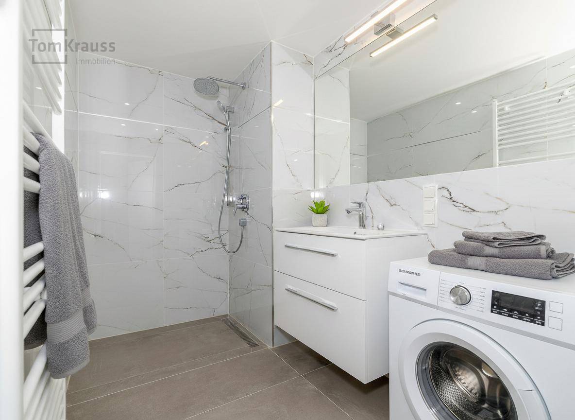 Modernes Badezimmer mit begehbarer Dusche, Waschbecken und Waschmaschine.